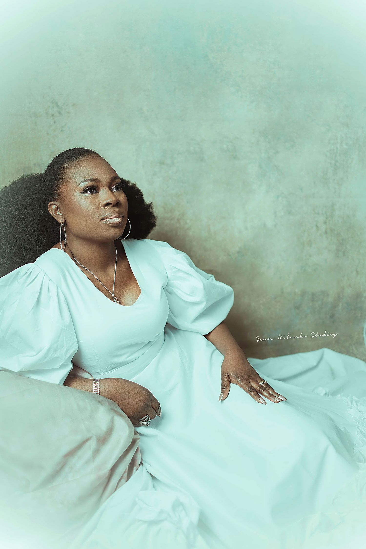 Artistic portrait in flowing white dress with puff sleeves against mint green backdrop.