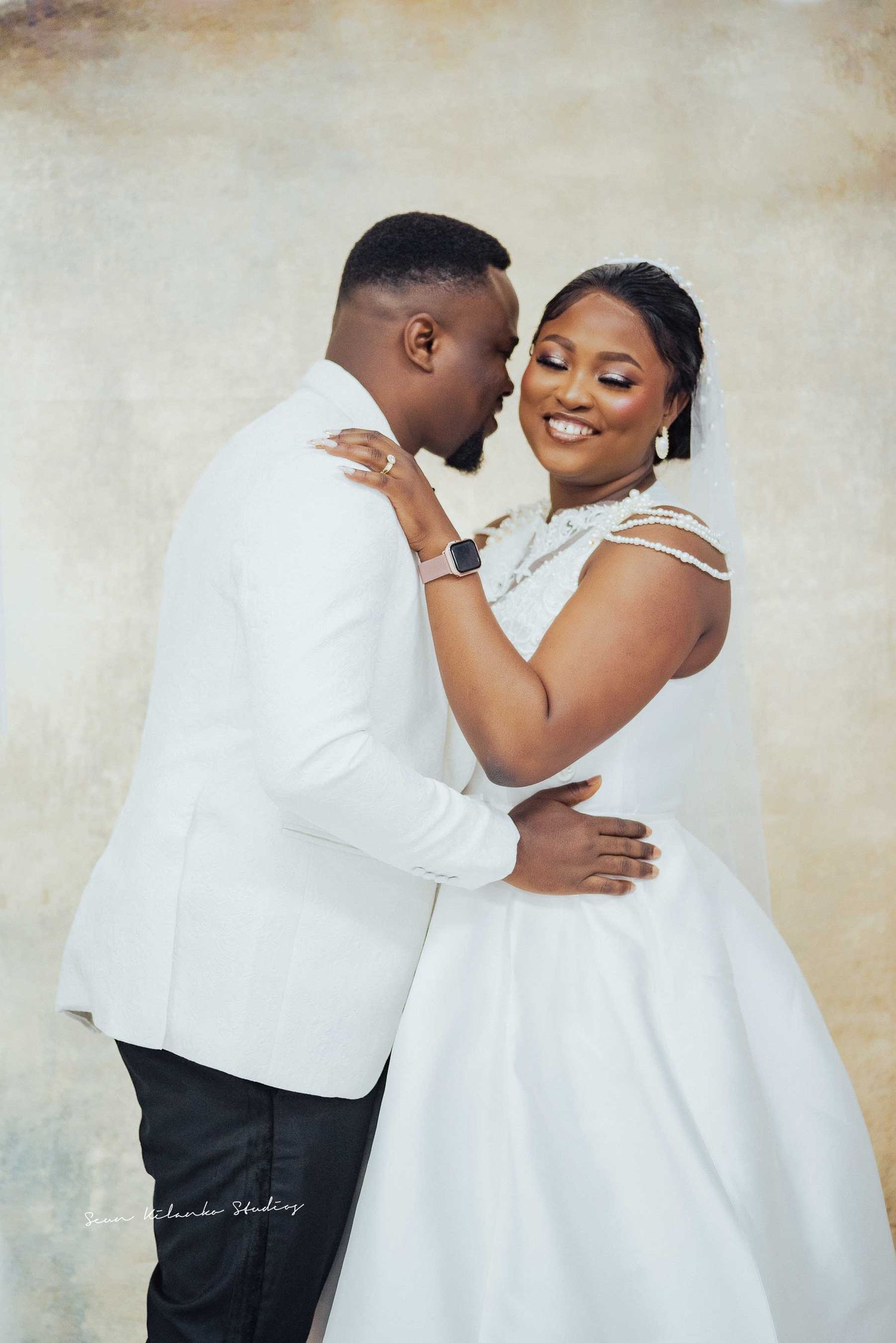 Romantic wedding portrait of couple embracing in white formal attire.