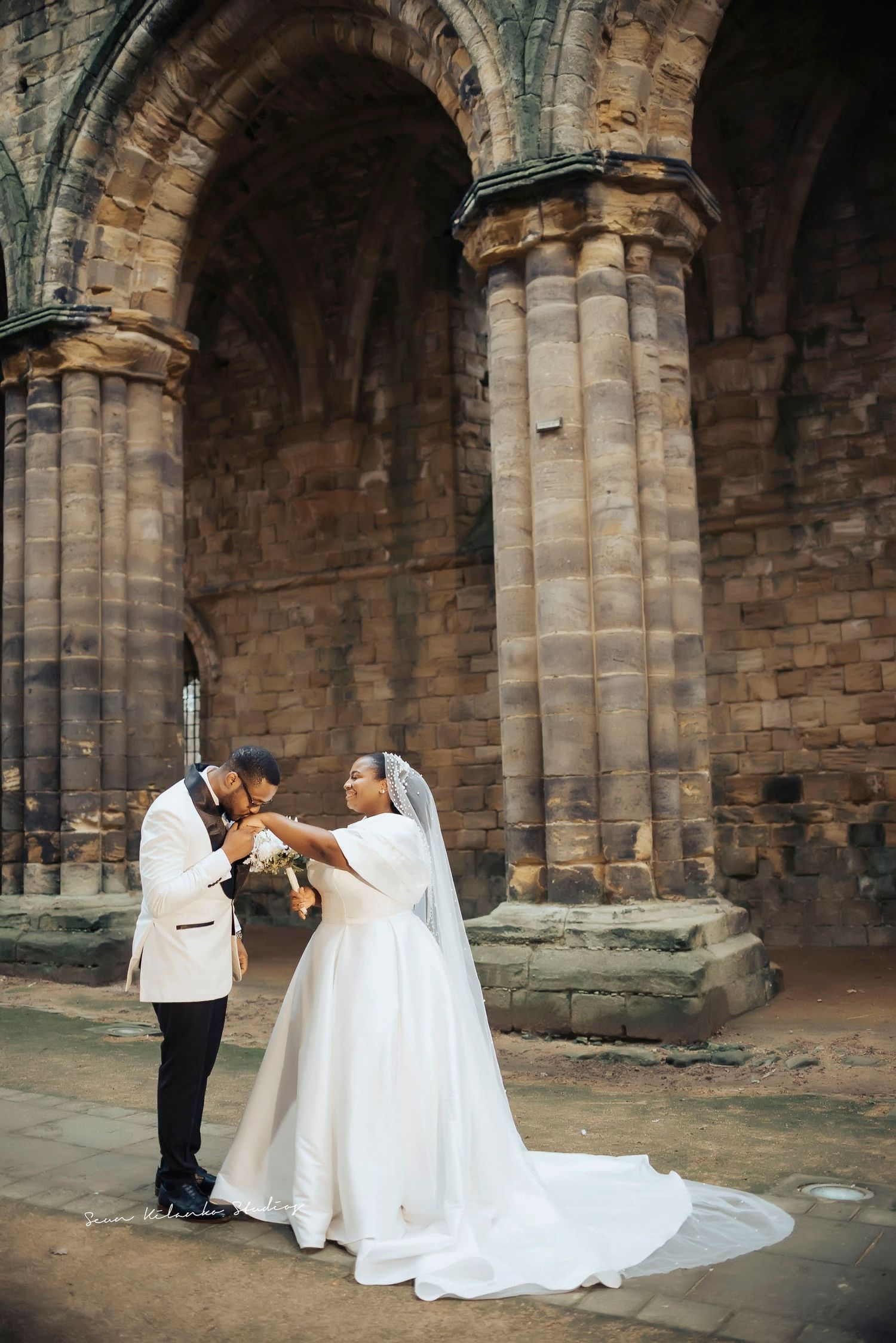 A tender wedding moment shared under majestic stone archways of an ancient cathedral.