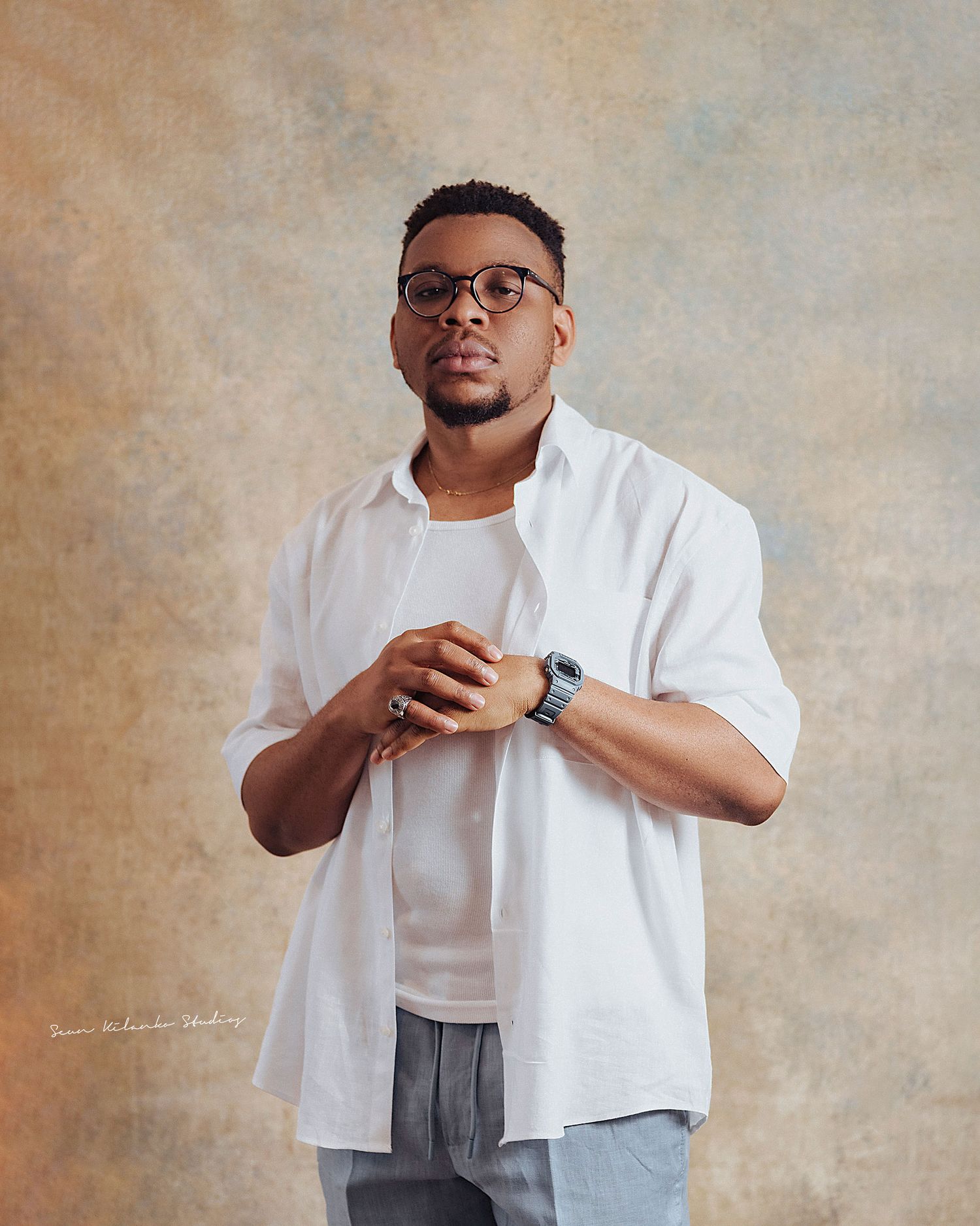Casual studio portrait of a person in layered white shirts and glasses against neutral background.