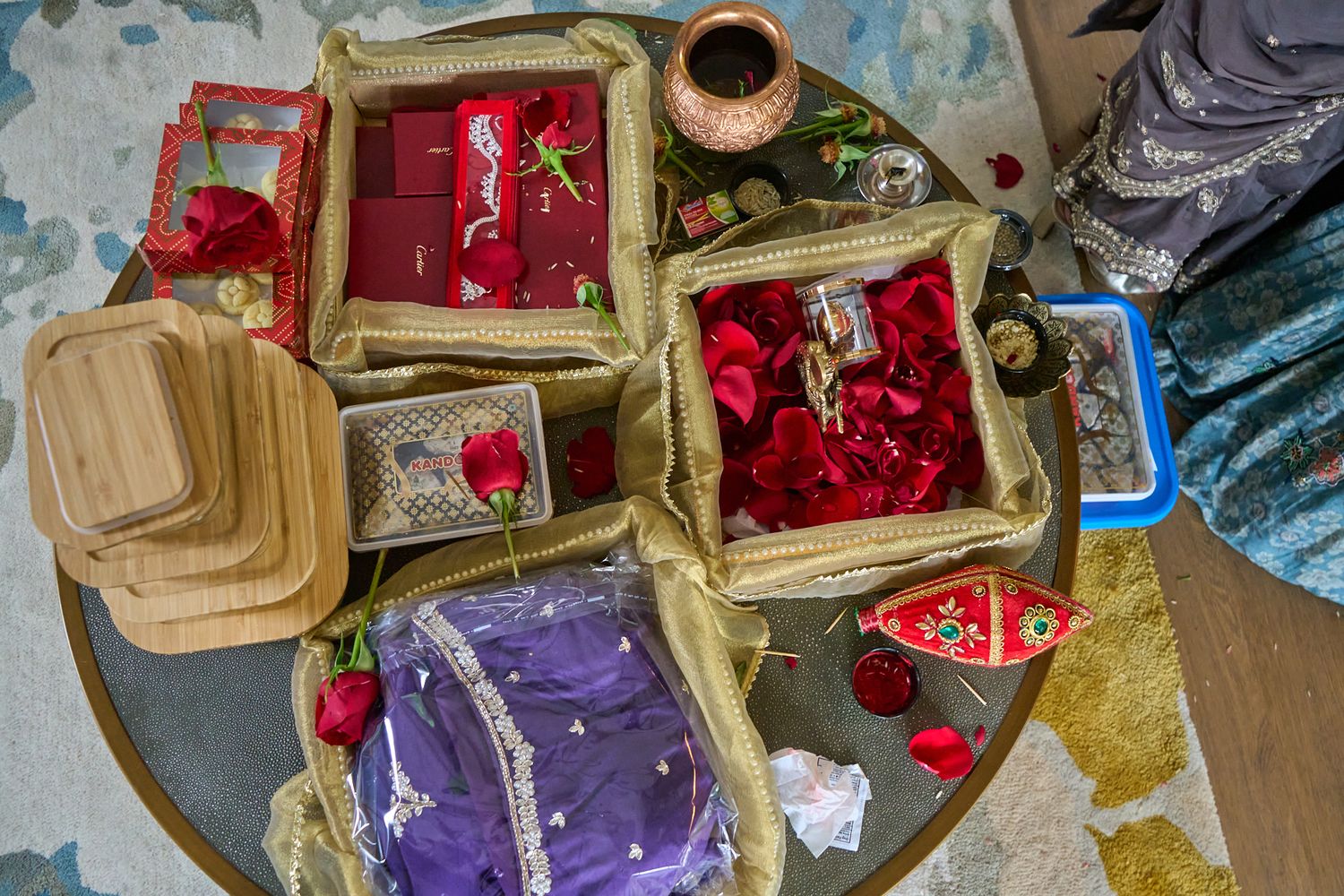 Overhead view of wedding ceremony items including red roses, wrapped gift boxes, a copper pot and a purple garment on a round table.