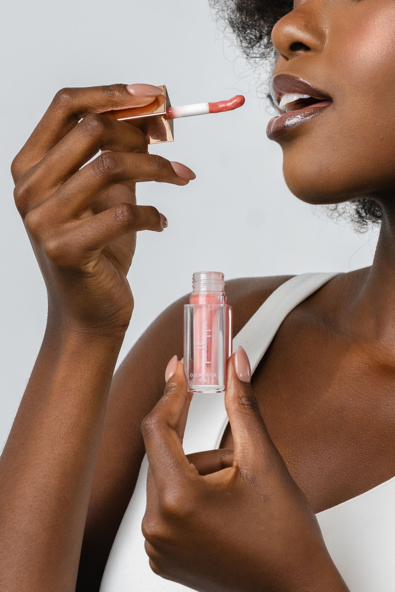 Woman applying pink lip gloss with wand applicator, holding clear bottle, beauty cosmetics product shot.