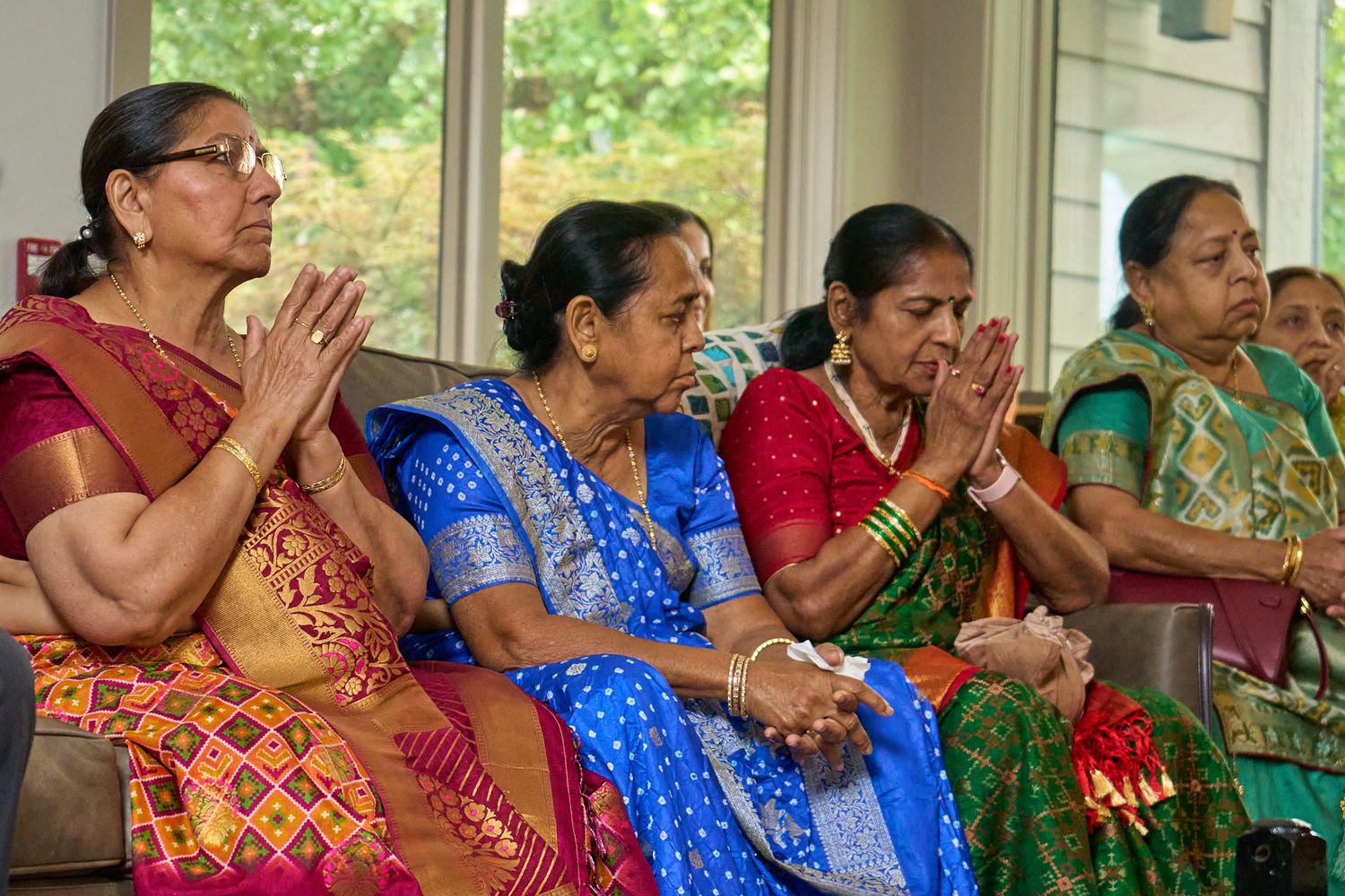 Indian women in colorful sarees praying with hands folded at a traditional Hindu ceremony.