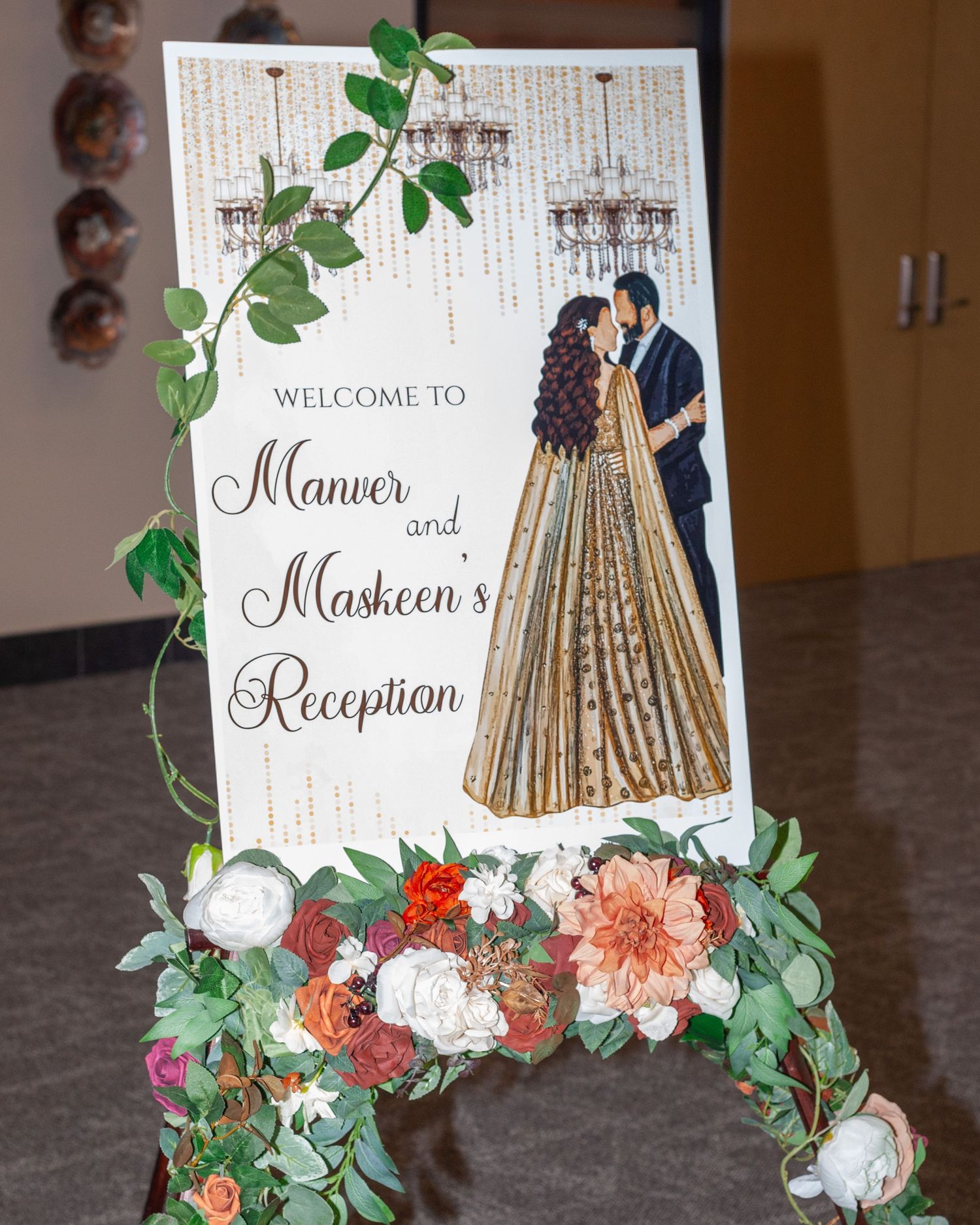 Welcome sign for Manver and Maskeen's wedding reception with an illustrated couple in a gold lehenga, framed by flowers and greenery.