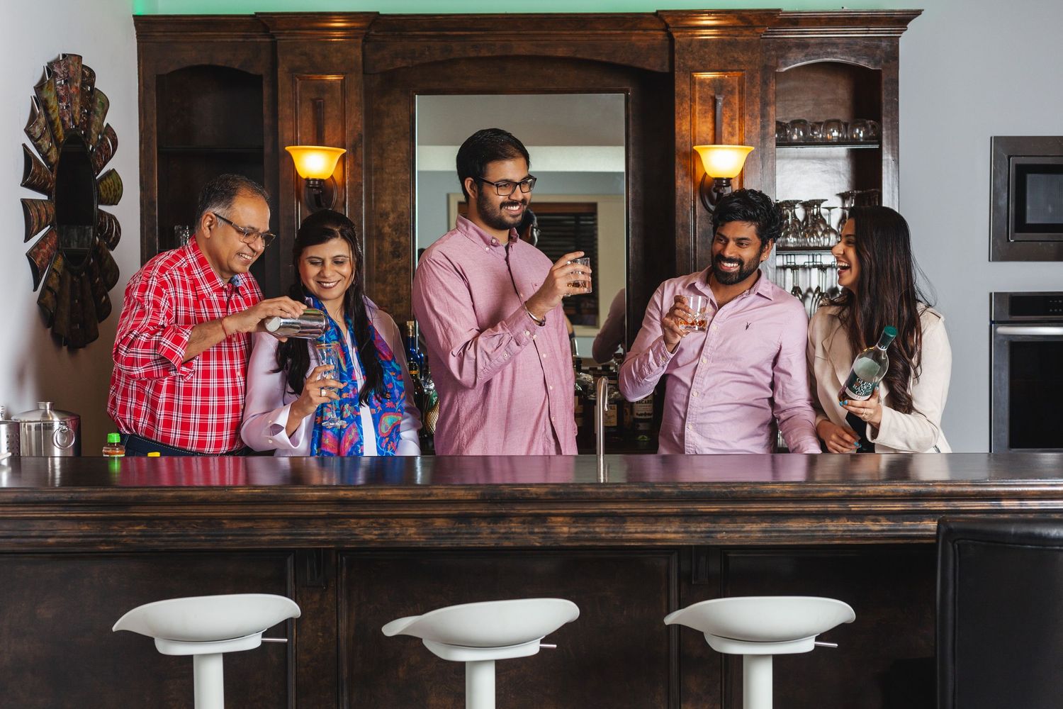 Group of five friends enjoying drinks together at a home bar counter with wooden cabinetry.