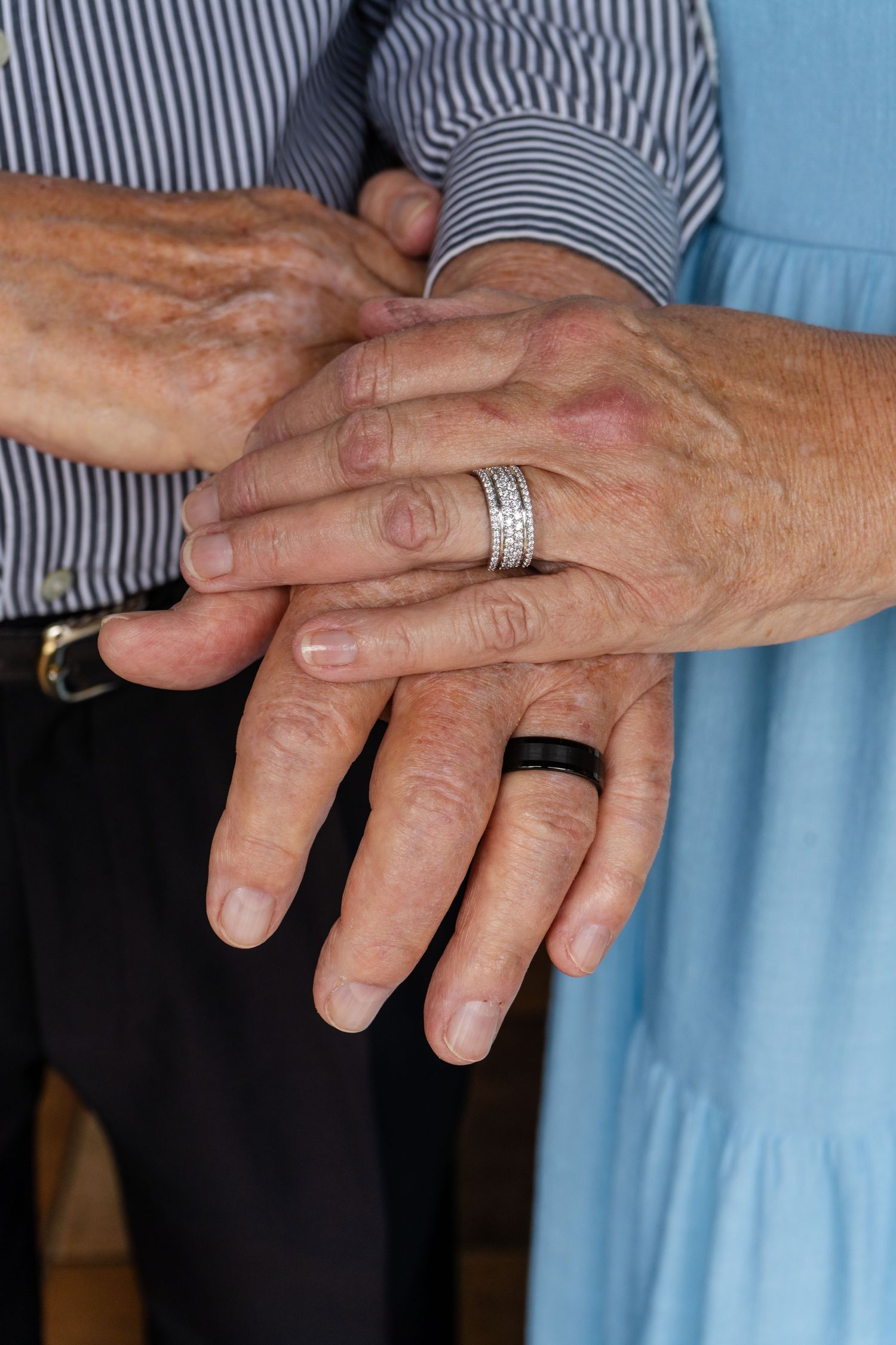 Close-up of elderly couple holding hands showing wedding rings in formal attire.
