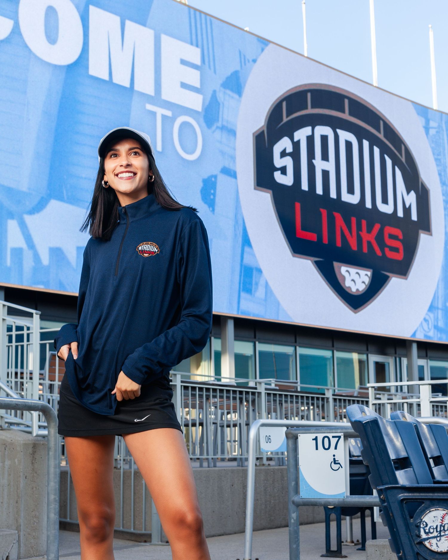 Woman in navy jacket poses at Stadium Links venue entrance with blue welcome signage.