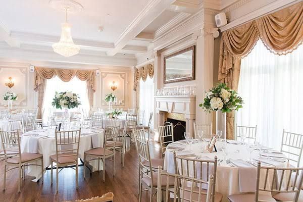 Elegant banquet room set for a wedding reception with white-clothed round tables, floral centerpieces, a crystal chandelier and gold drapes.