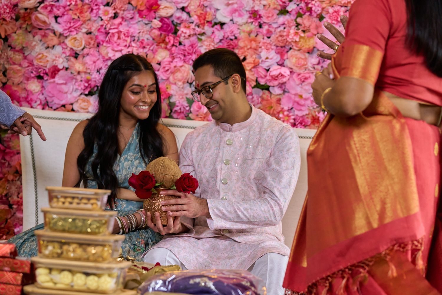 Couple in traditional South Asian attire seated at a vibrant floral backdrop during a wedding ceremony.