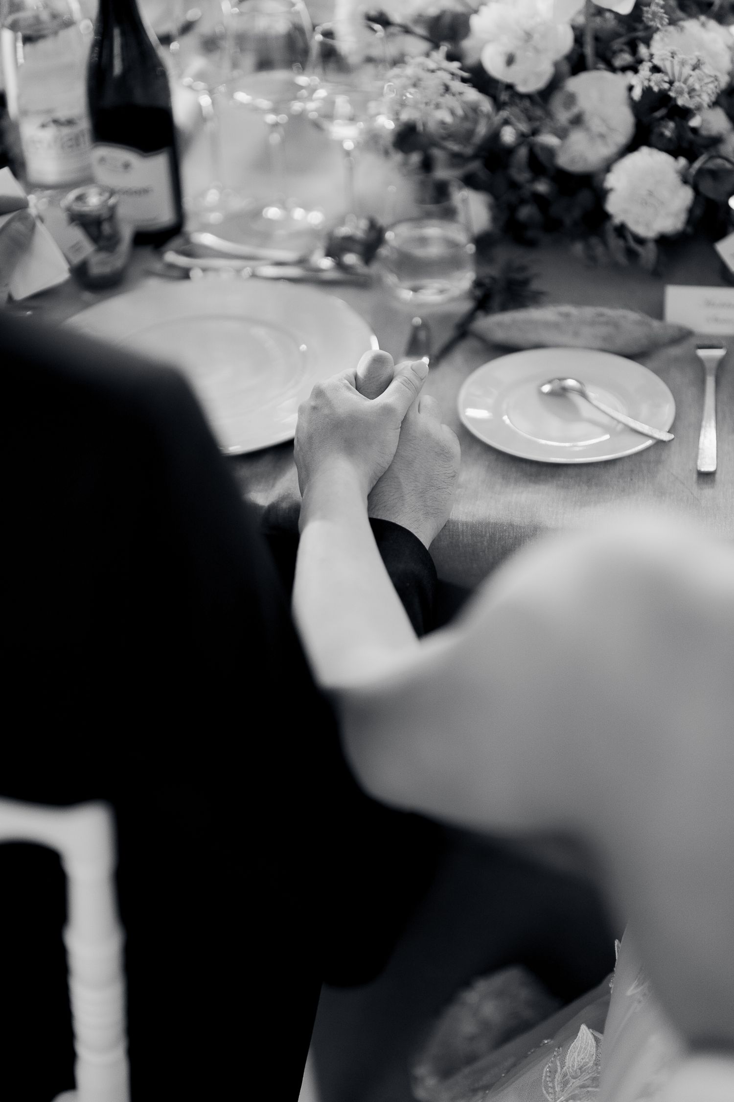 Black and white photo of a formal dinner table setting with wine glasses, plates and floral centerpiece decorations.
