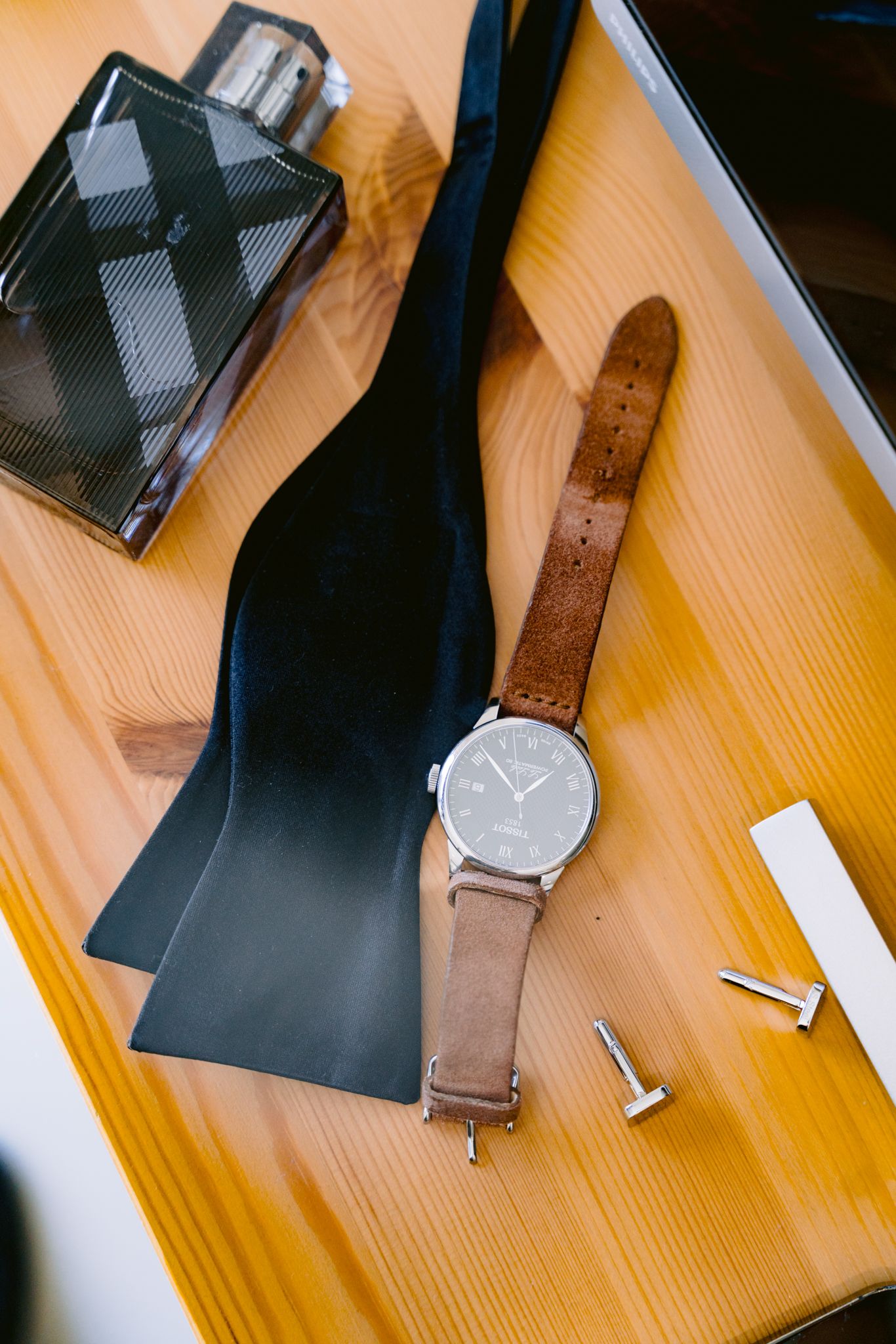 A brown leather watch band and black device components laid out on a wooden surface in sequential order.