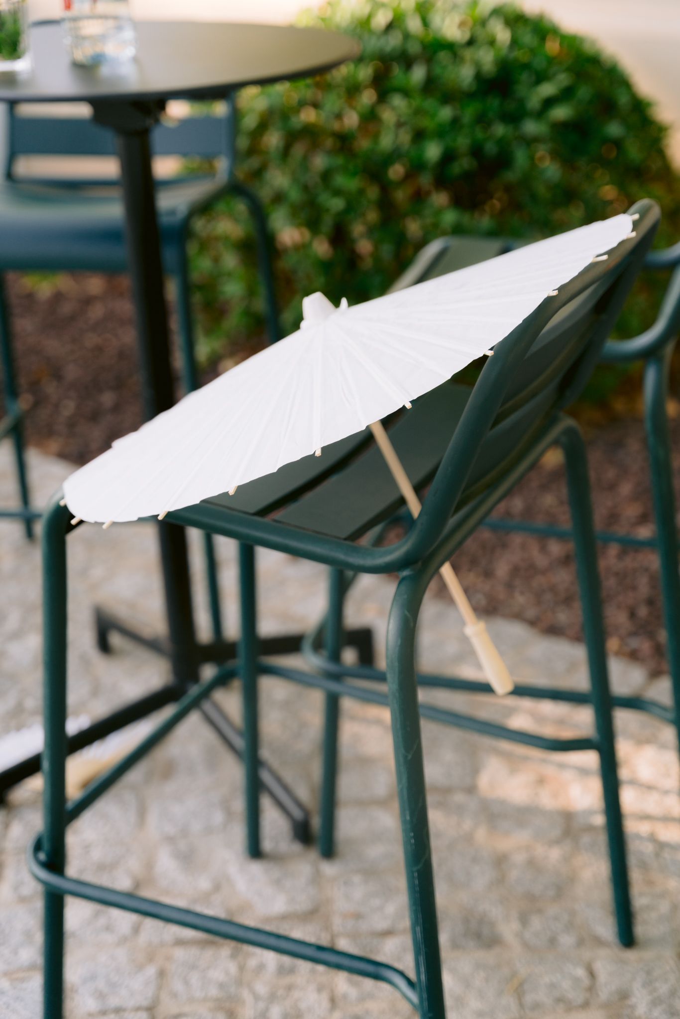 White paper parasols rest atop green metal chairs in an outdoor garden setting.