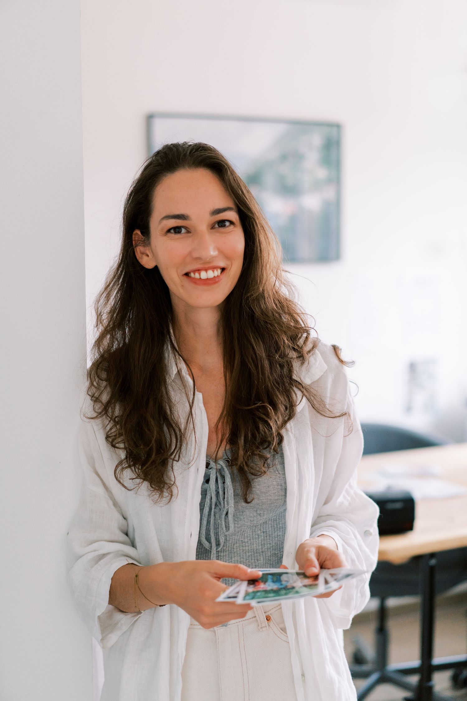 Professional woman in white blazer and gray top smiling in modern office setting.
