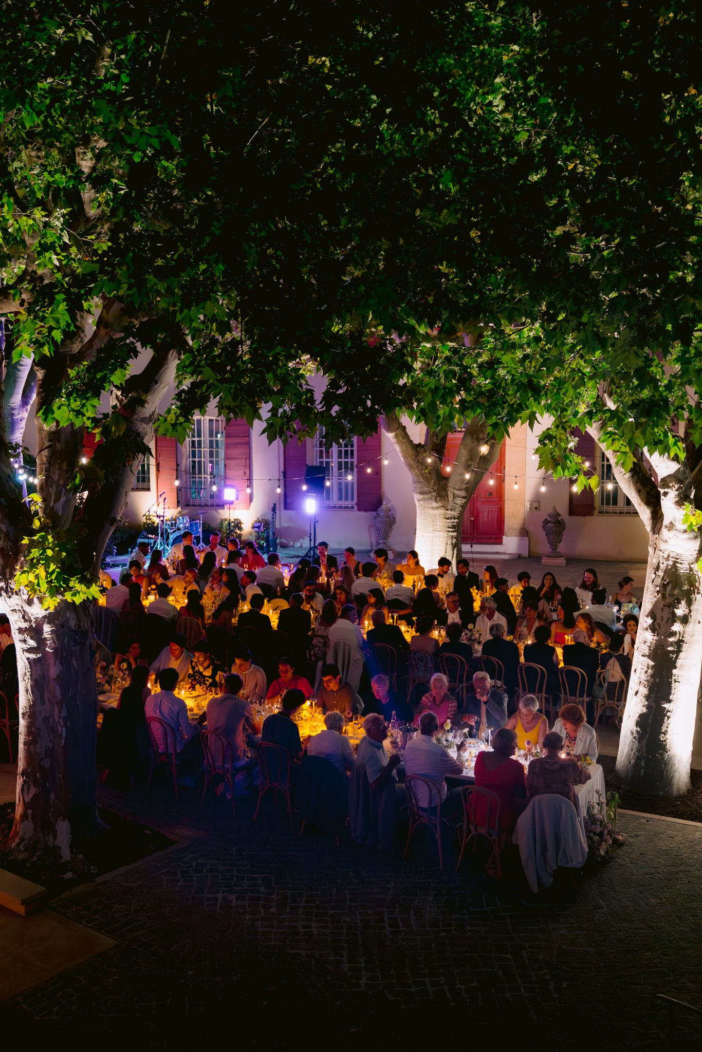 A large crowd gathers outdoors at night under illuminated trees during an evening event.
