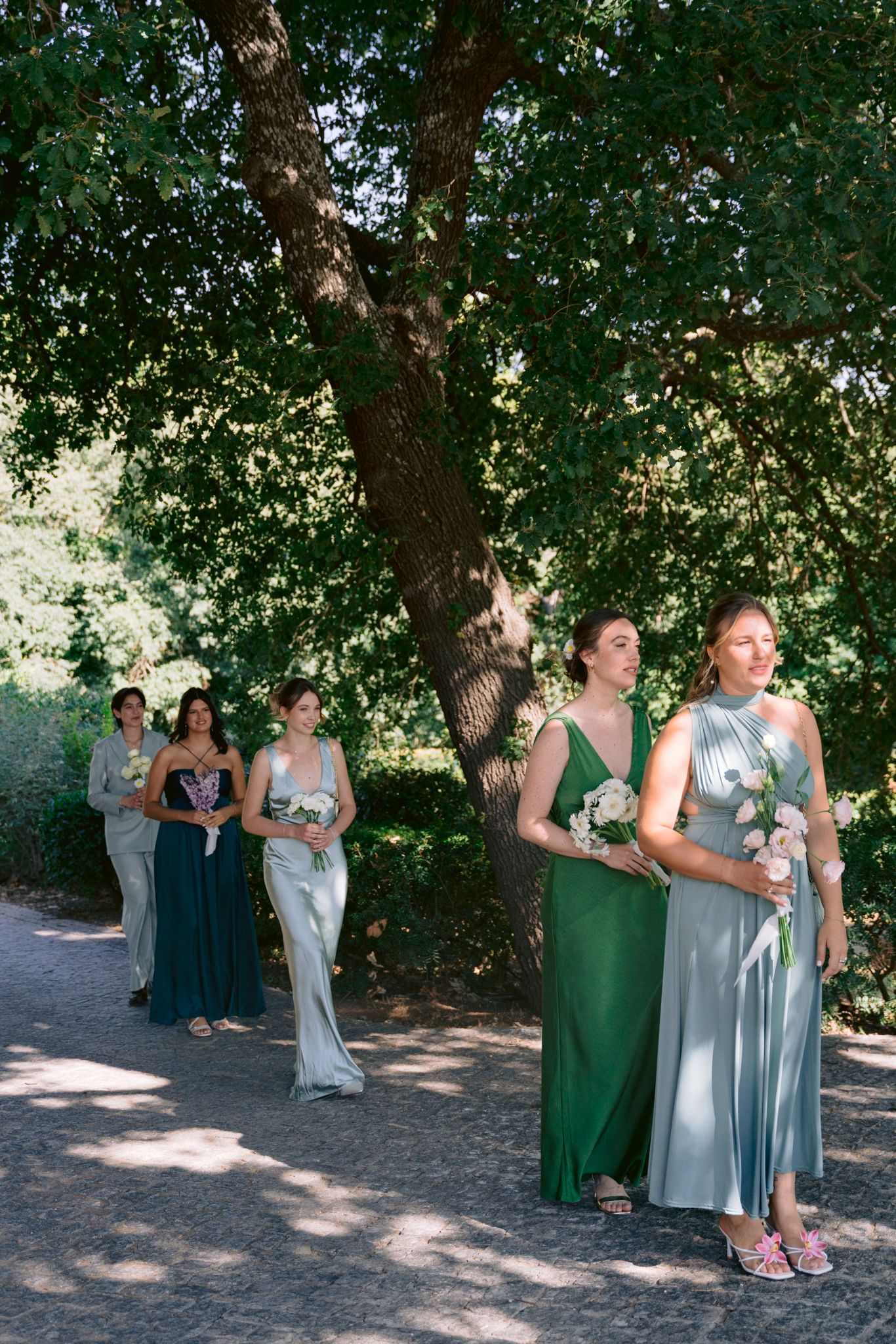 A group stands together under shady trees during an outdoor celebration wearing green and light blue dresses.