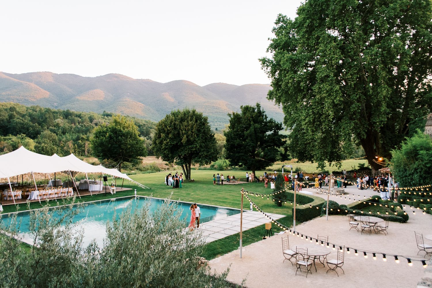 Outdoor wedding reception by a pool with white tents, mountain views, and lush greenery in a scenic venue.
