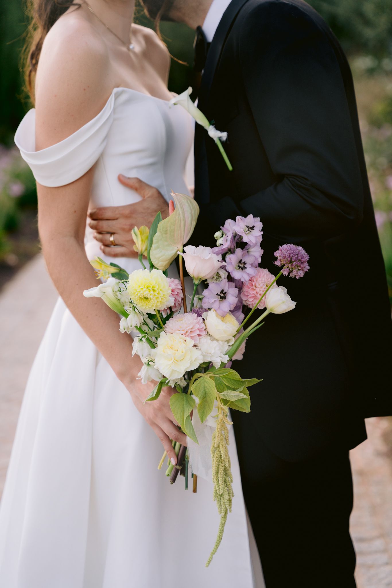 A romantic wedding photo showing a couple embracing with a delicate bouquet of pink and yellow flowers.