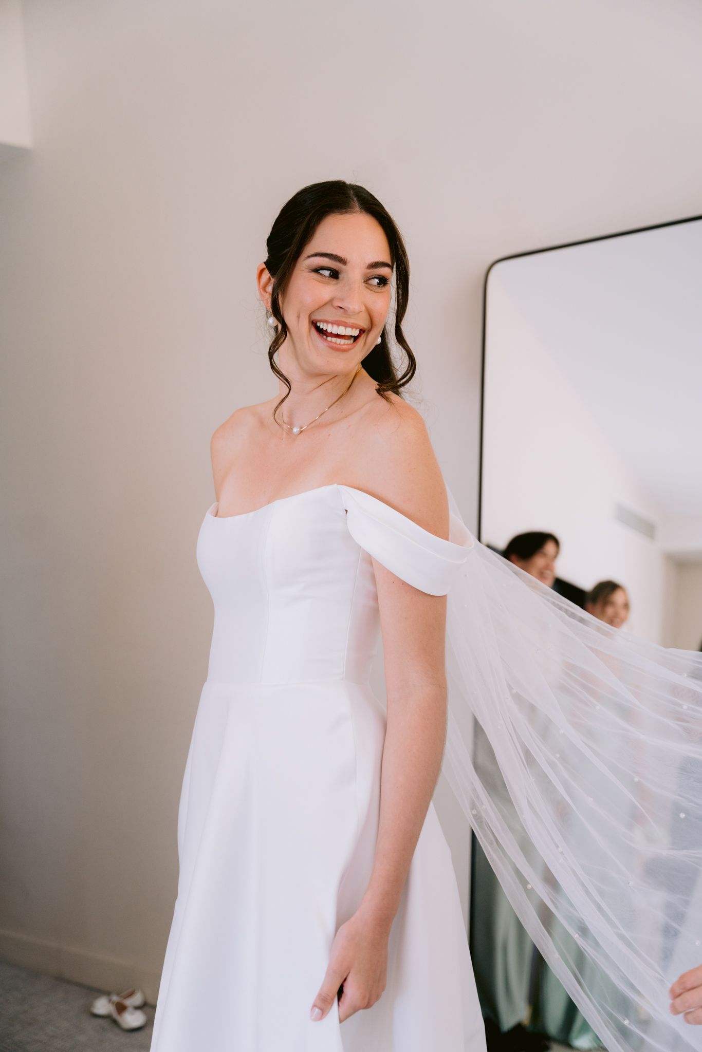 A white bridal gown with off-shoulder design and cathedral veil captured in a bright indoor setting.