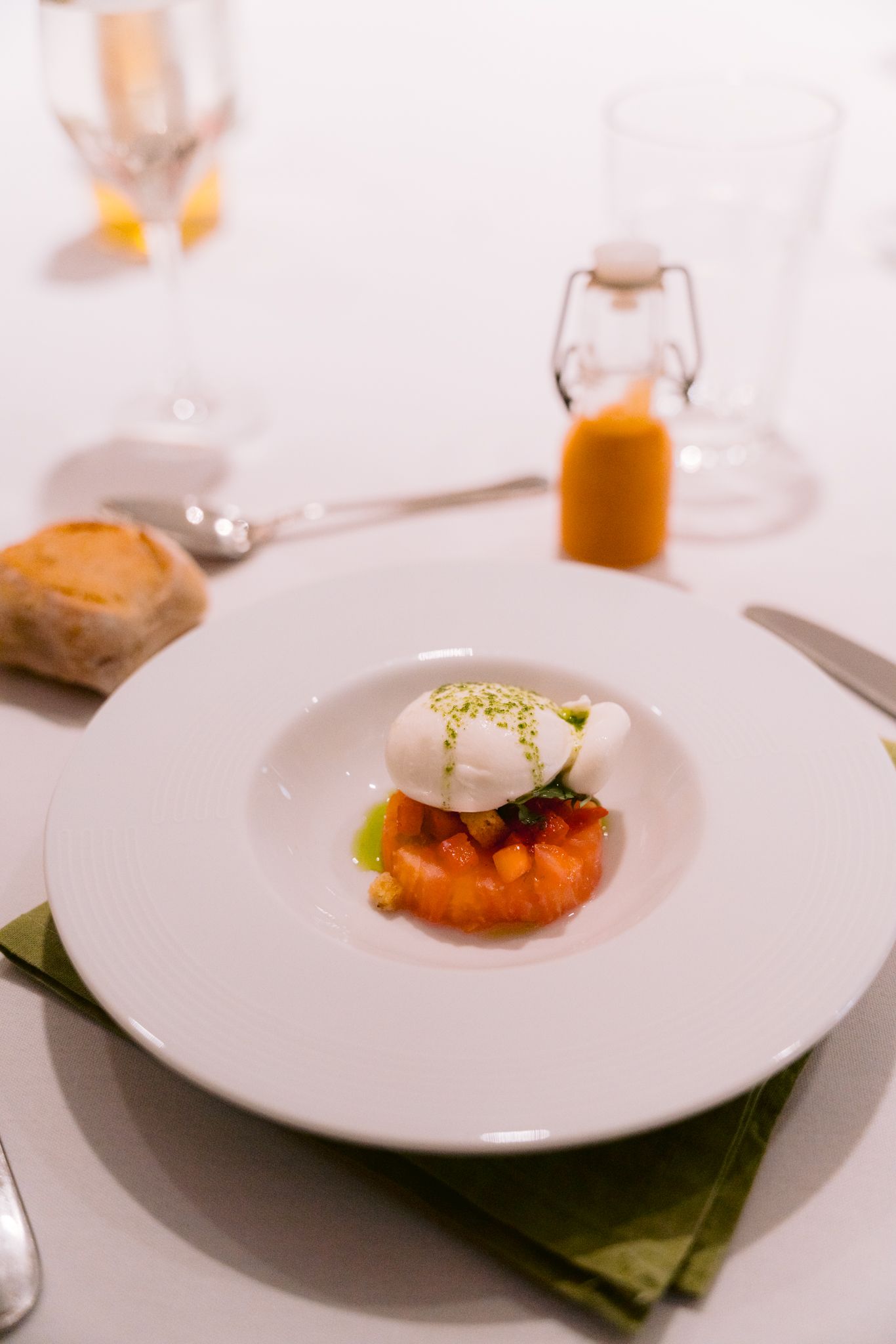 Elegant plated dish featuring poached egg over salmon tartare on a white plate with a bottle of orange sauce in background.