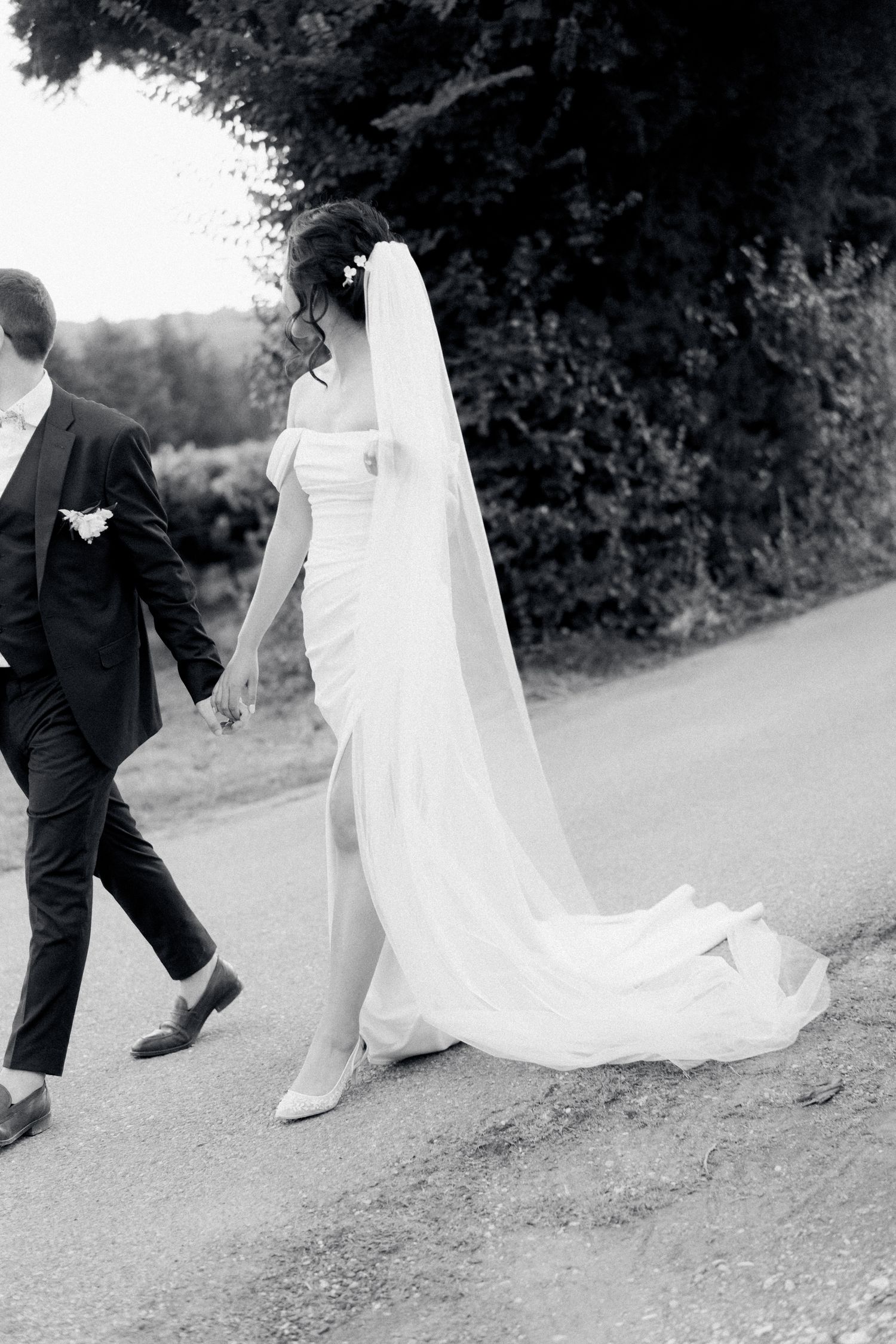 Classic black and white wedding photo showing elegant bridal gown with flowing train on country path.
