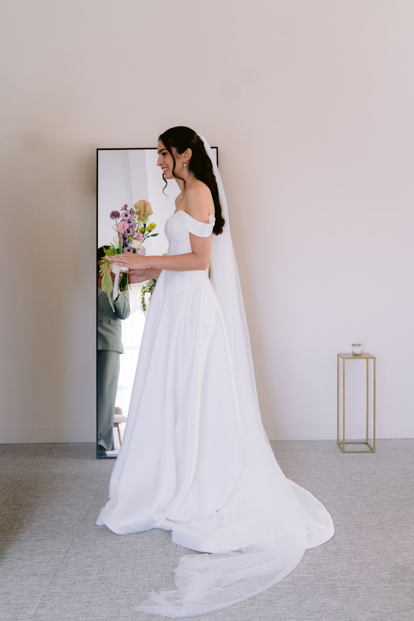 A flowing white wedding gown with off-shoulder details and long train shown from different angles in a minimalist setting.