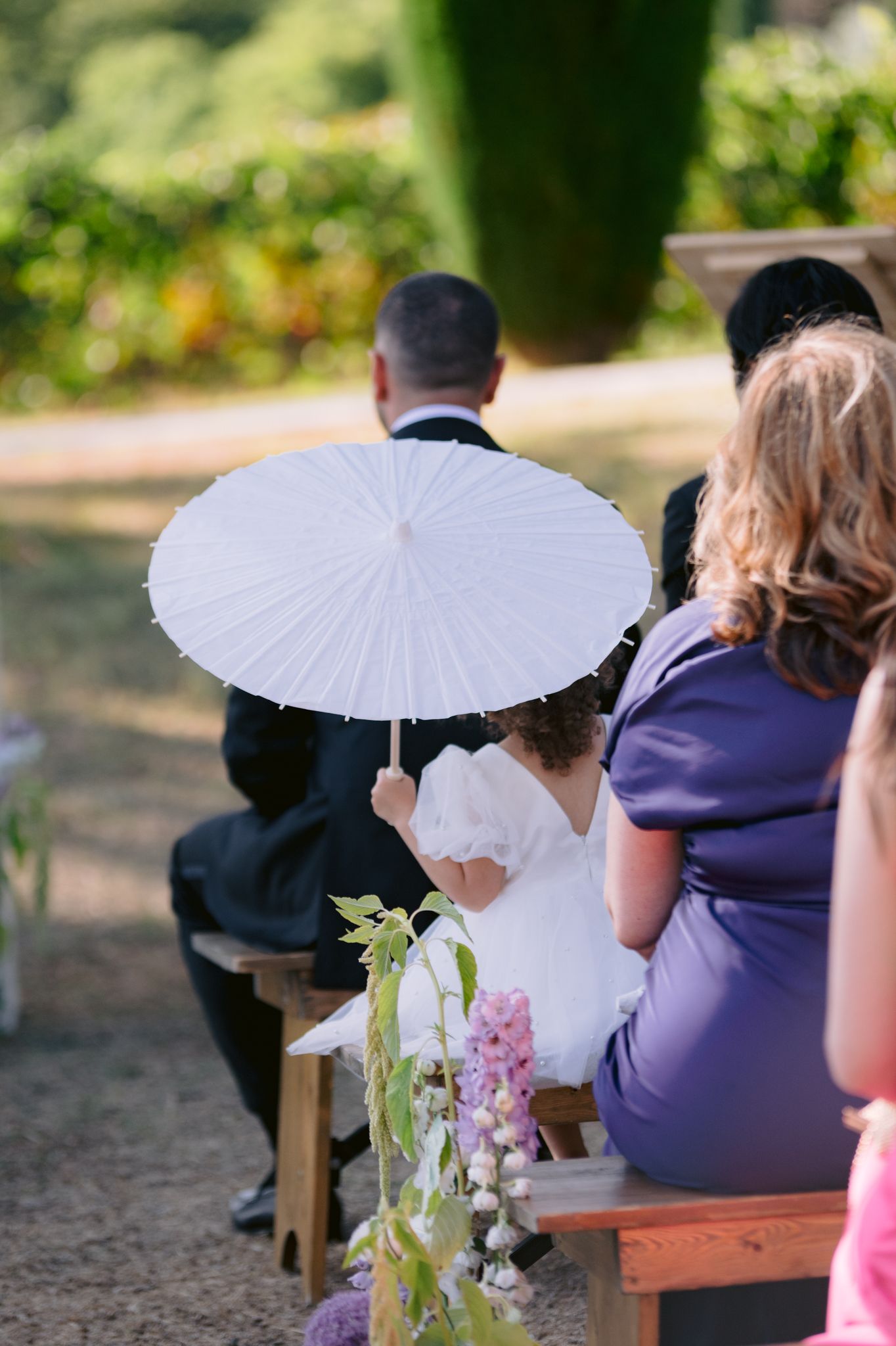 White parasol and floral decorations accent outdoor wedding ceremony seating arrangement.