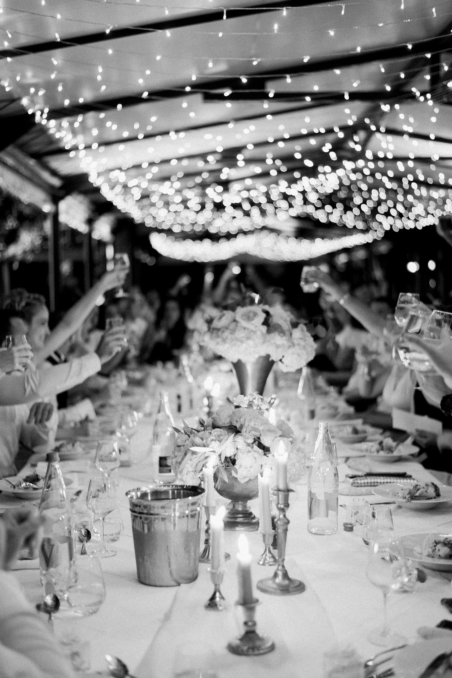 Elegant wedding reception table under twinkling fairy lights with candles and glassware.