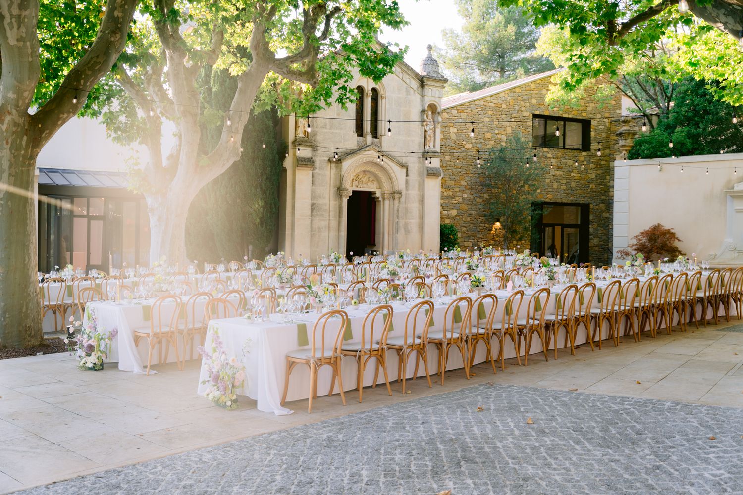 Elegant outdoor wedding venue with stone walls and wooden chairs arranged in rows for a ceremony in natural sunlight.