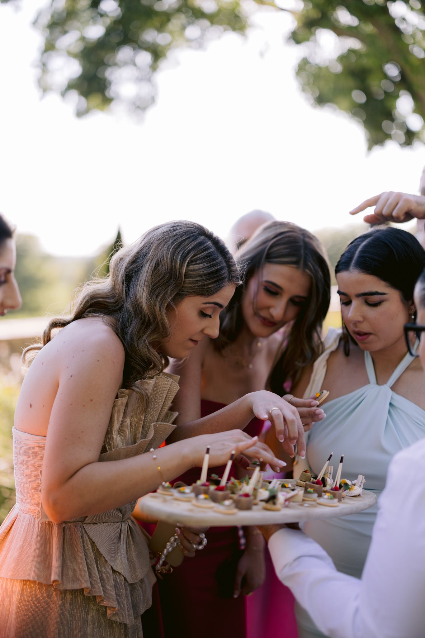 A group of guests enjoying appetizers from a tray at an outdoor event during golden hour.