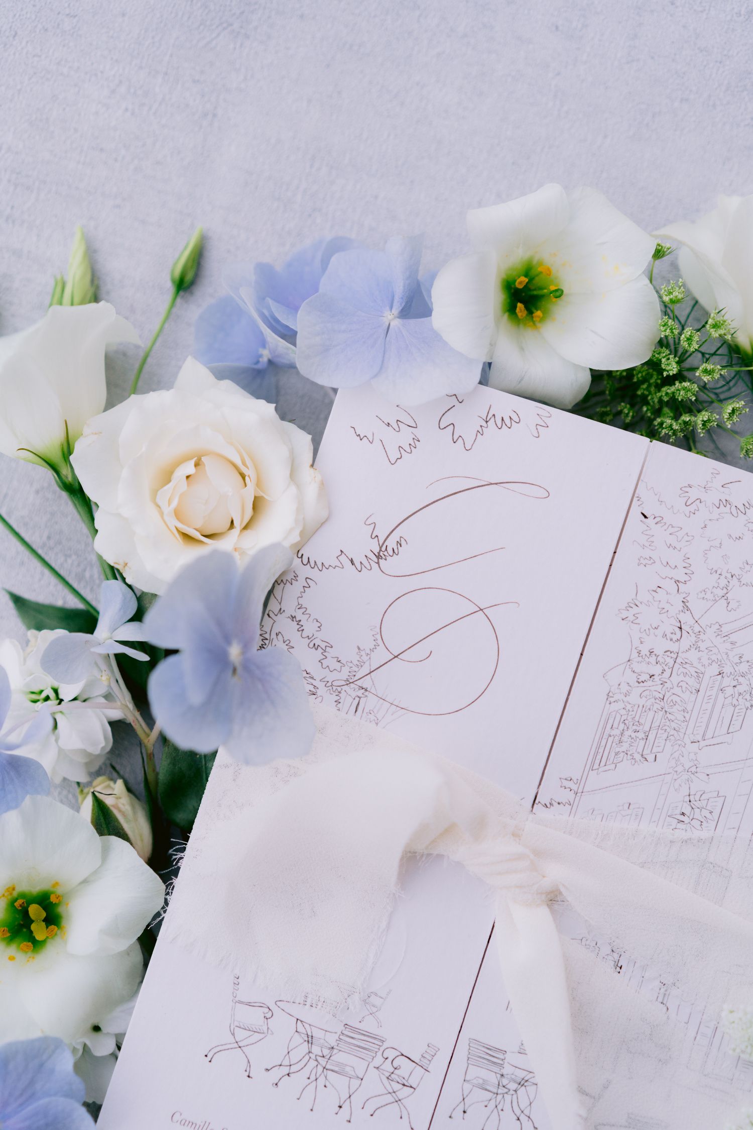 Delicate floral arrangement with white roses and blue hydrangeas alongside wedding stationery.