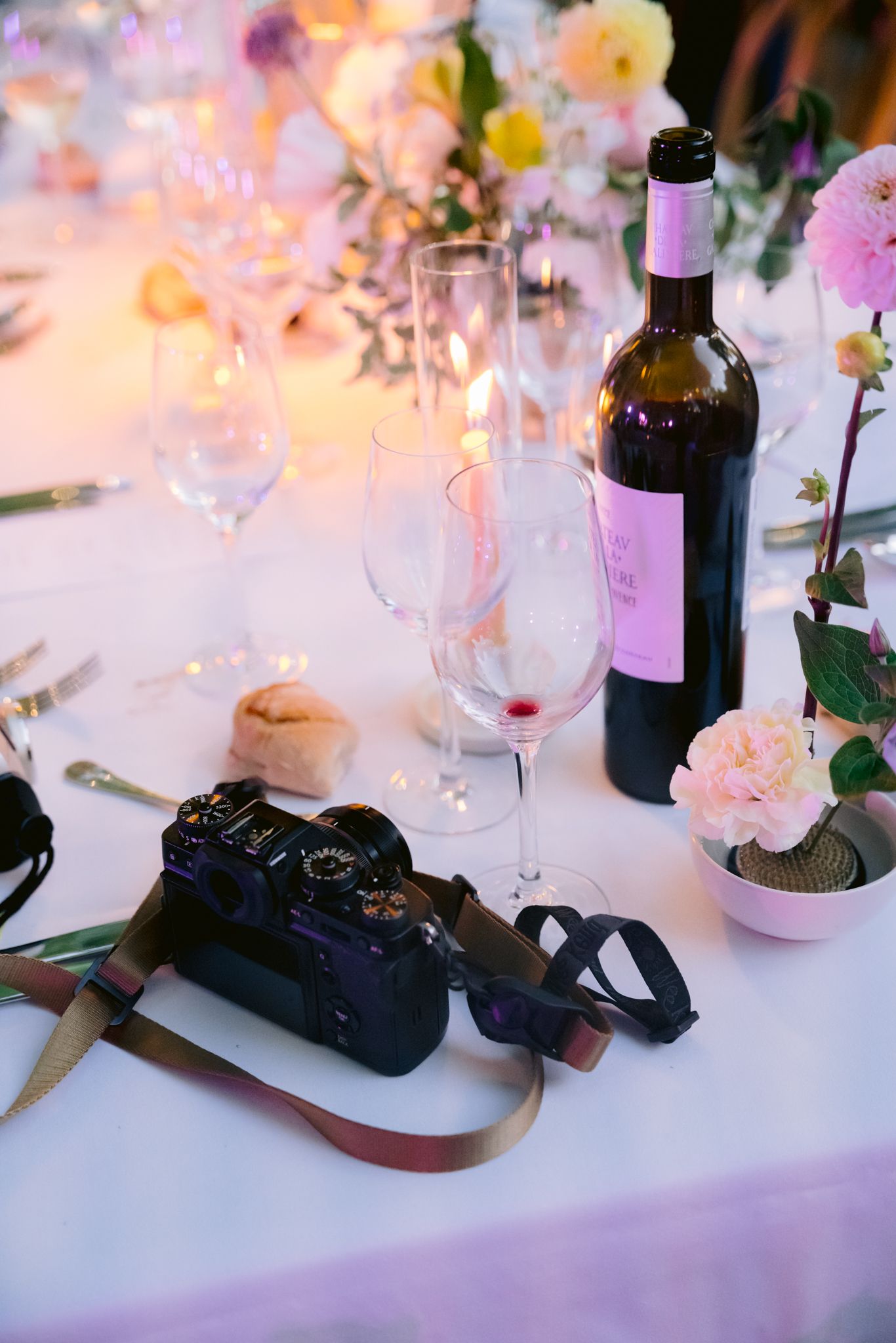 A vintage camera sits among wine bottles and glassware on an elegantly decorated table with soft lighting and flowers.