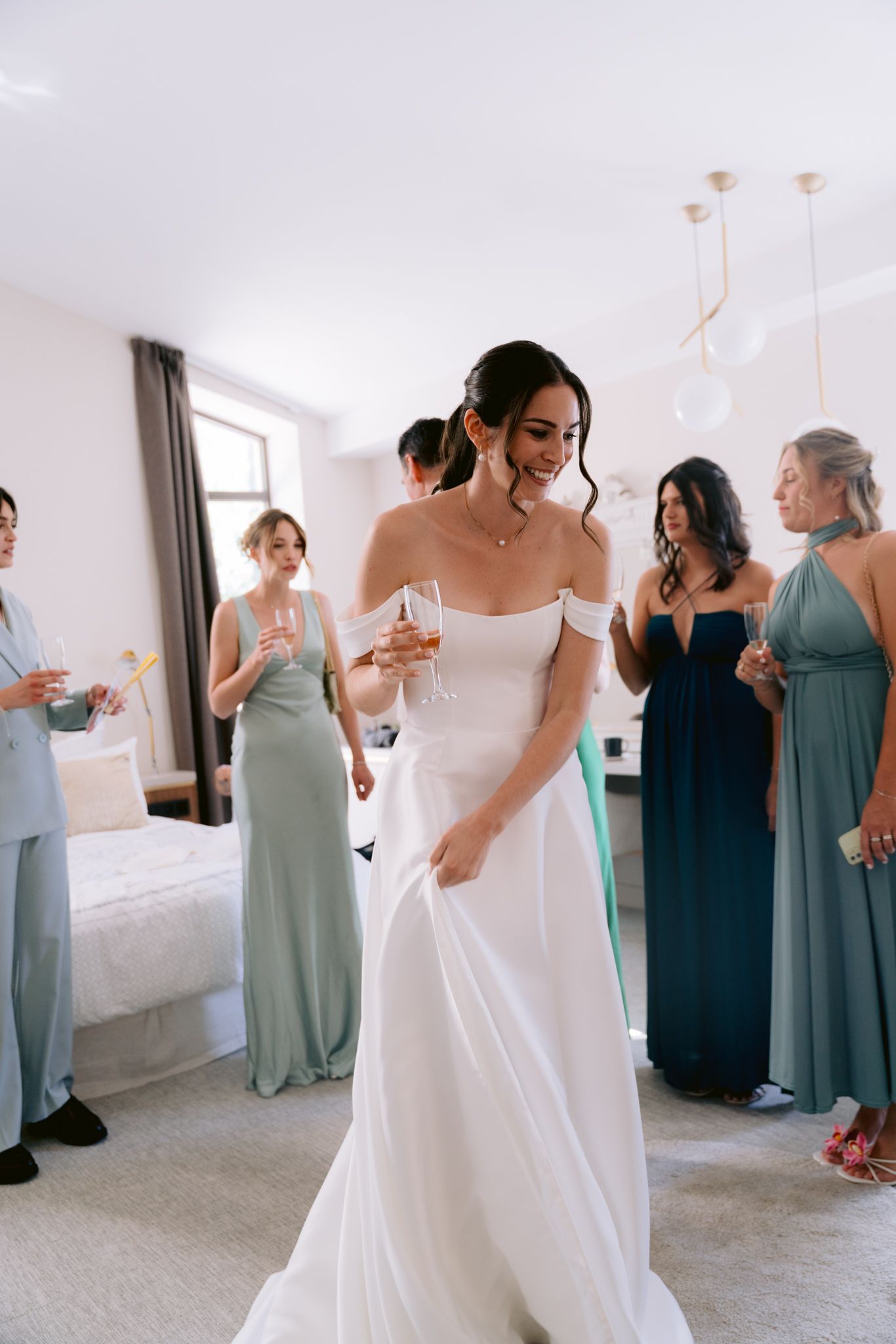 Wedding party members in navy and sage green dresses gather around a bride in white during pre-ceremony preparations.