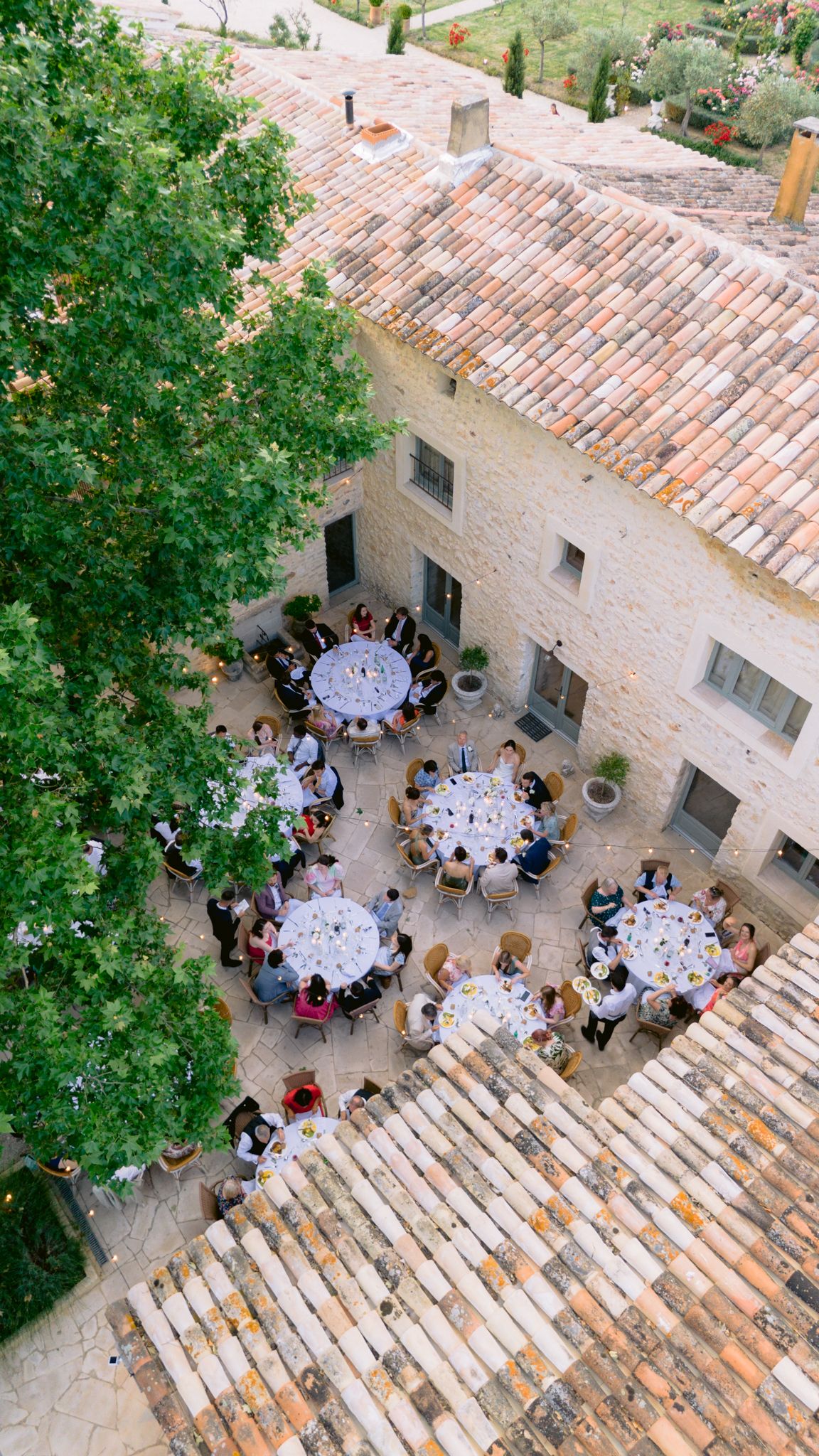 Aerial view of an elegant outdoor wedding reception with round tables in a rustic stone courtyard.