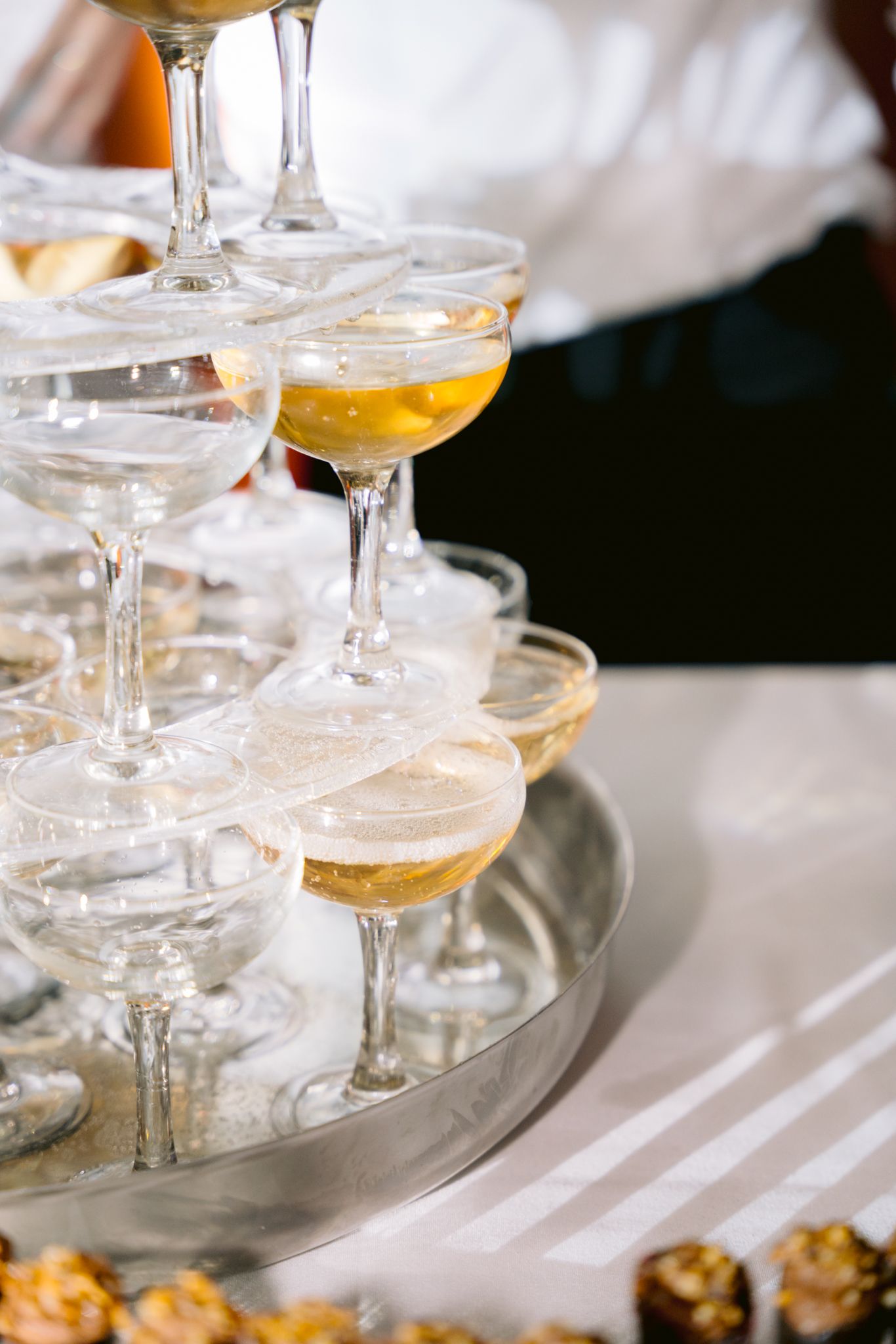 Elegant champagne glasses arranged in rows on white tablecloth with soft natural lighting and shallow depth of field.