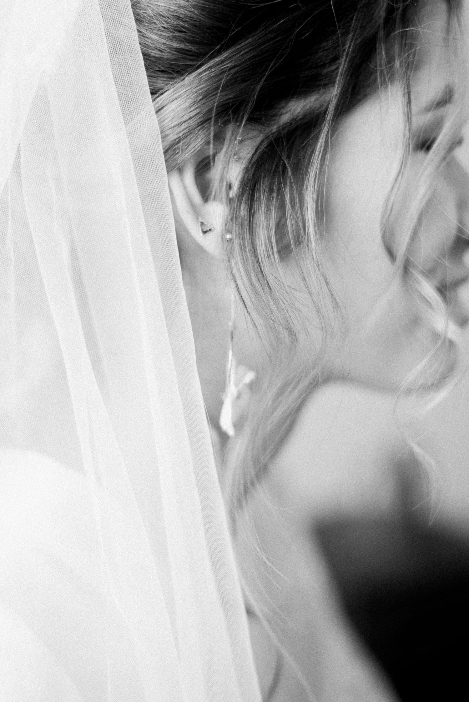 Black and white close-up of a bride wearing a delicate veil and drop earring, with soft flowing hair on her wedding day.