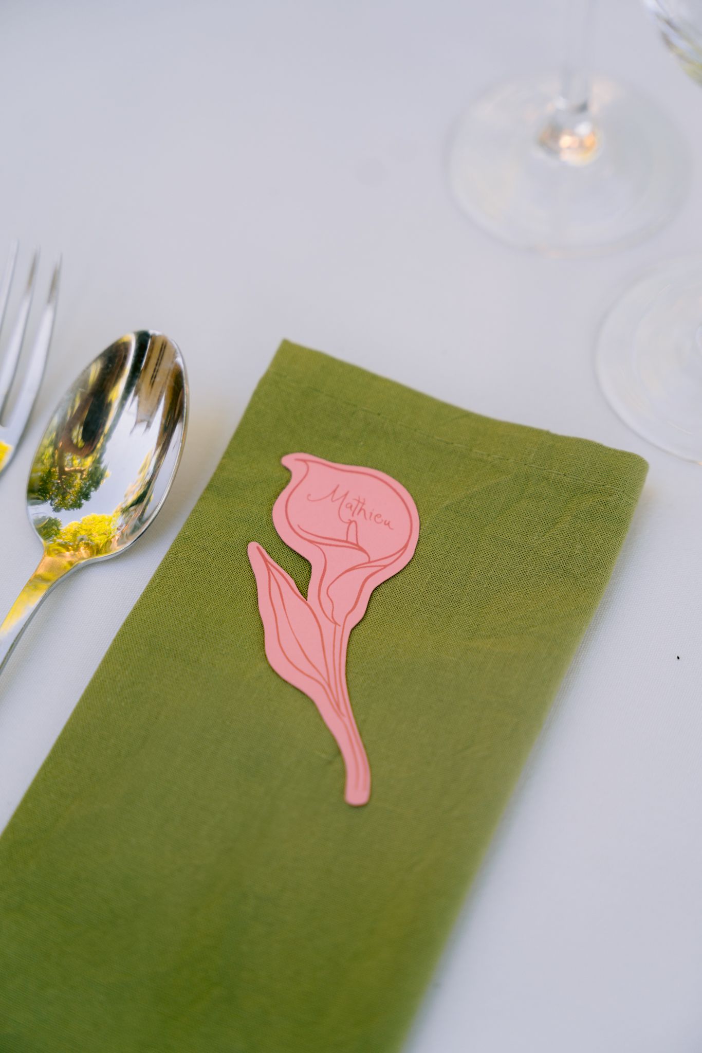 Pink napkin holders shaped like flamingos rest on green cloth napkins arranged on a white table setting.