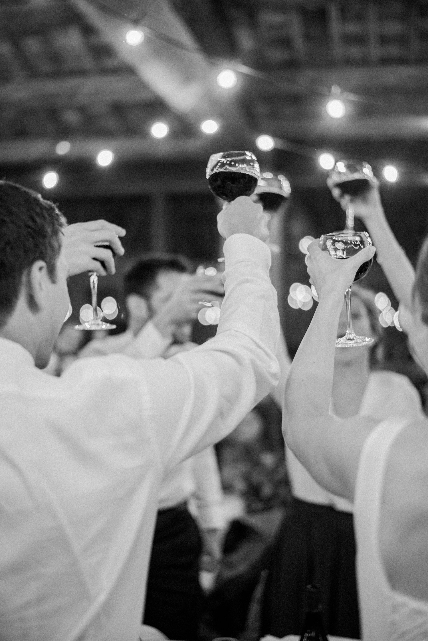 Black and white photo of guests raising wine glasses in a toast at an elegant evening celebration.