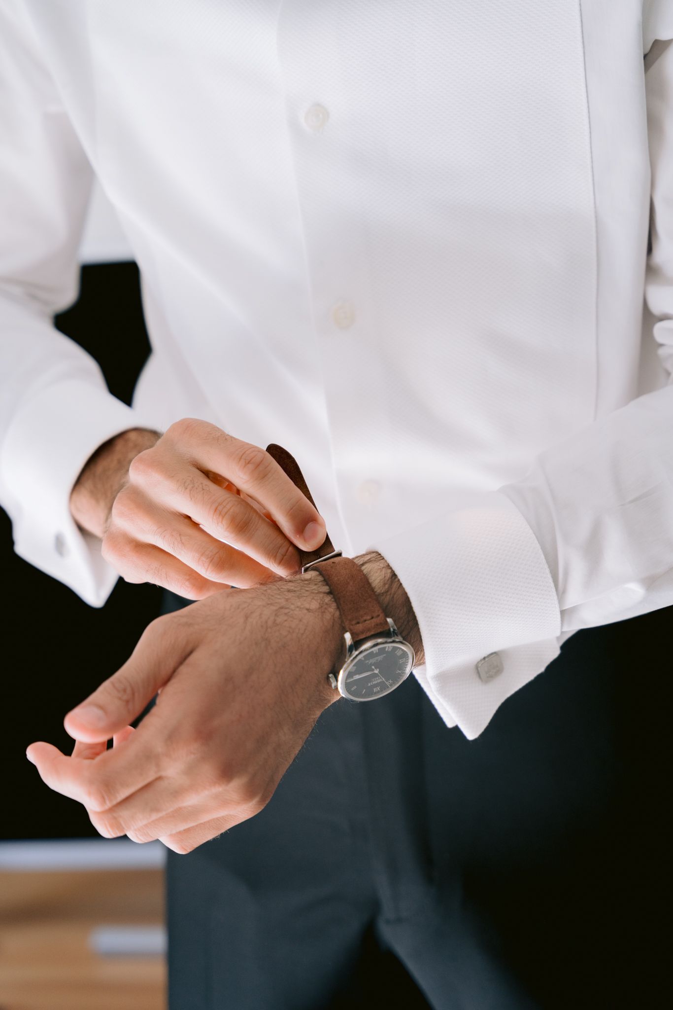 Close-up of hands adjusting a sleek wristwatch while wearing a crisp white dress shirt and dark suit.