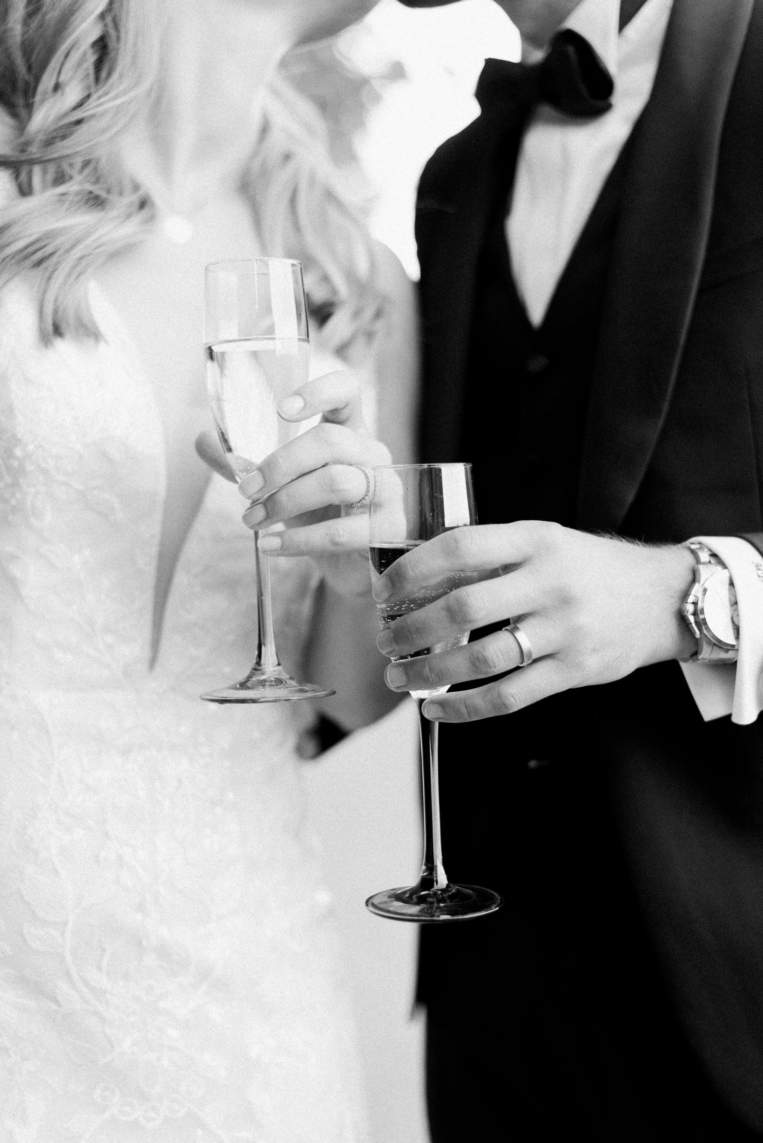 Black and white photo of a bride and groom holding champagne flutes, wearing wedding rings, celebrating their marriage.
