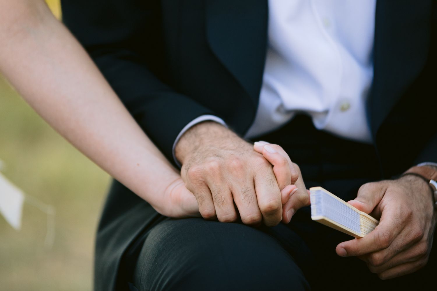 Close-up of two people holding hands while one person holds a smartphone, wearing formal attire.