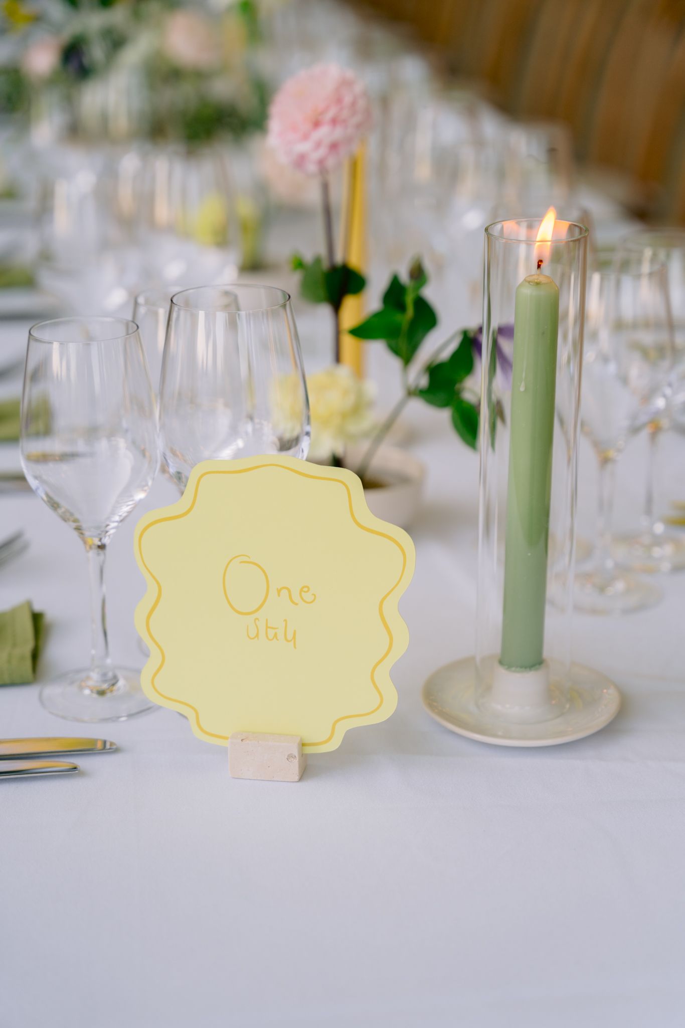 Wedding table settings with pale yellow name cards, green taper candles, and crystal glassware on white tablecloths.