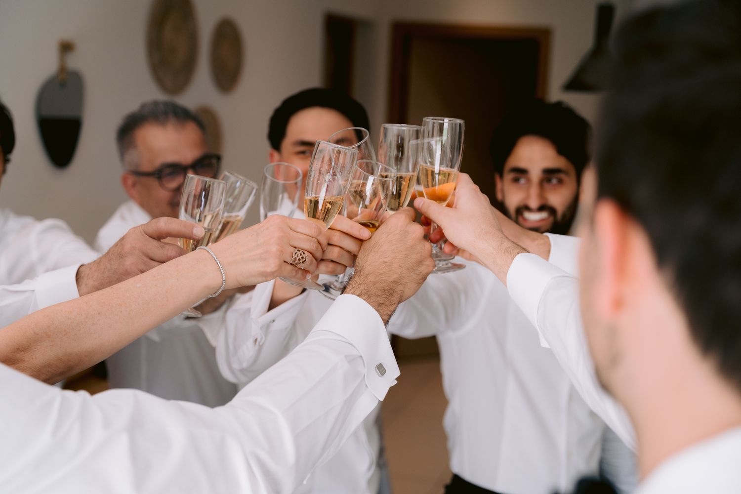 A group in white shirts raise their glasses together in a celebratory toast at an indoor gathering.