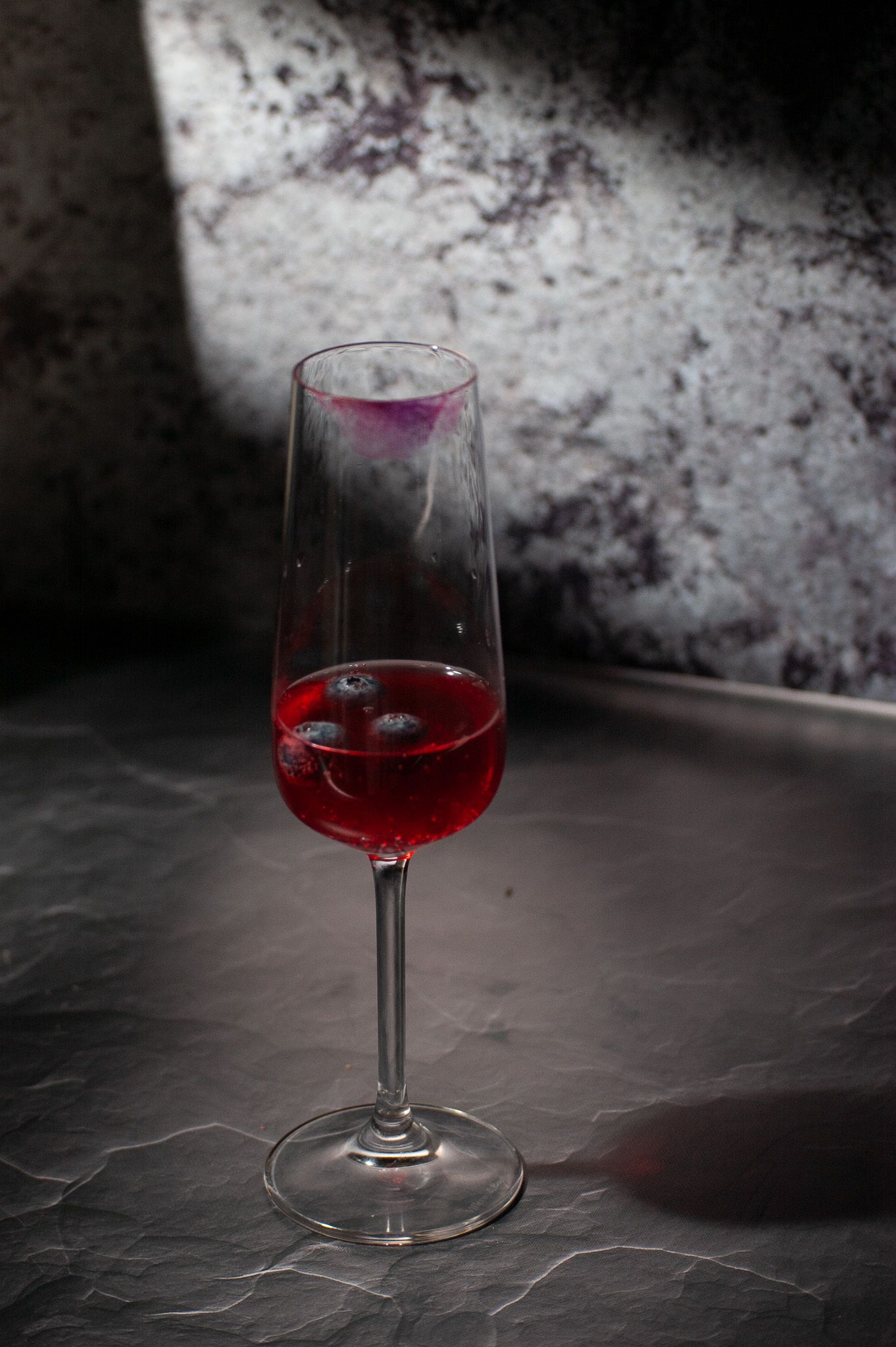 A single glass of vibrant red wine on a dark textured surface against a moody, distressed background.