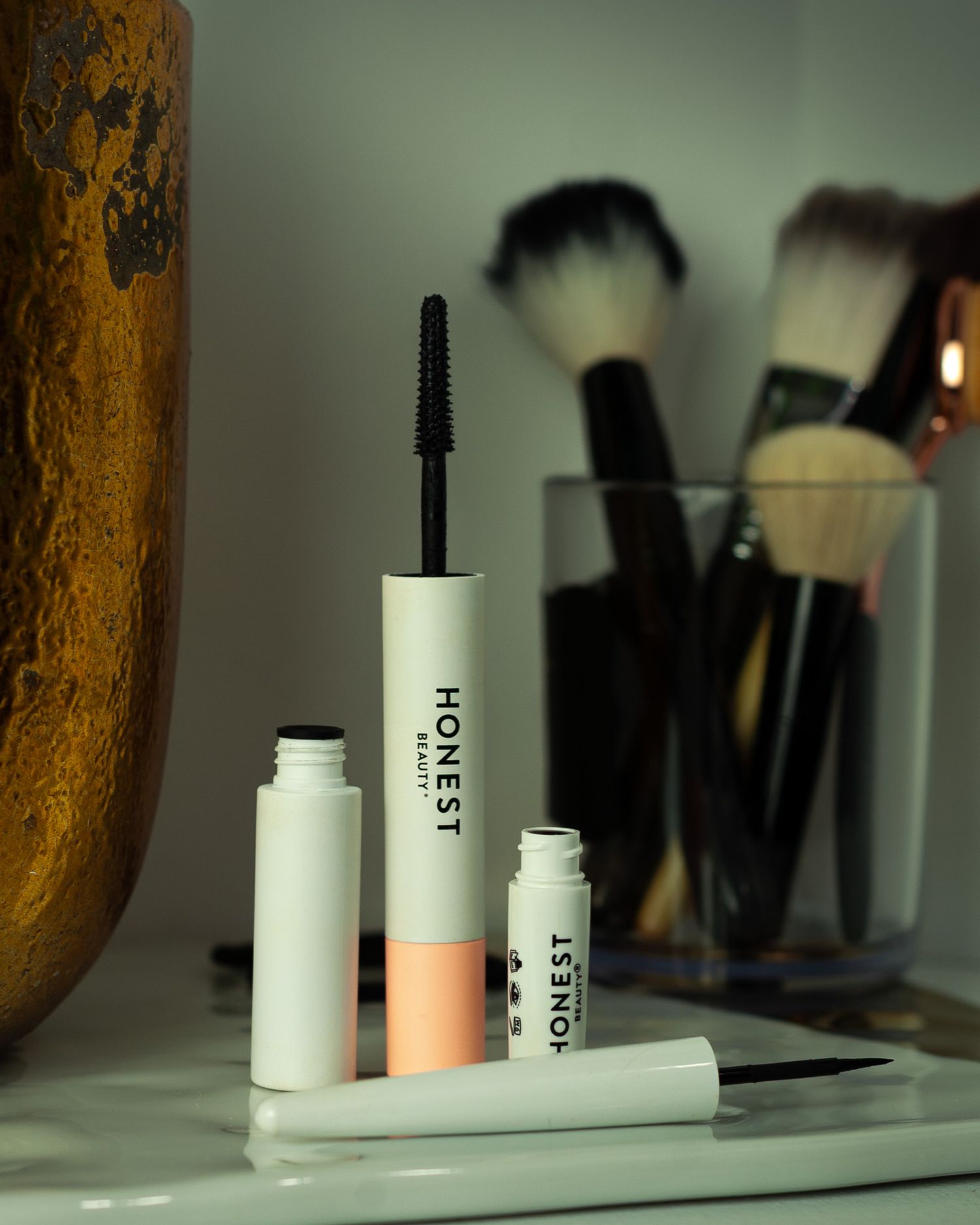 Makeup products including mascara and brushes arranged on a white surface with beauty tools visible in background.