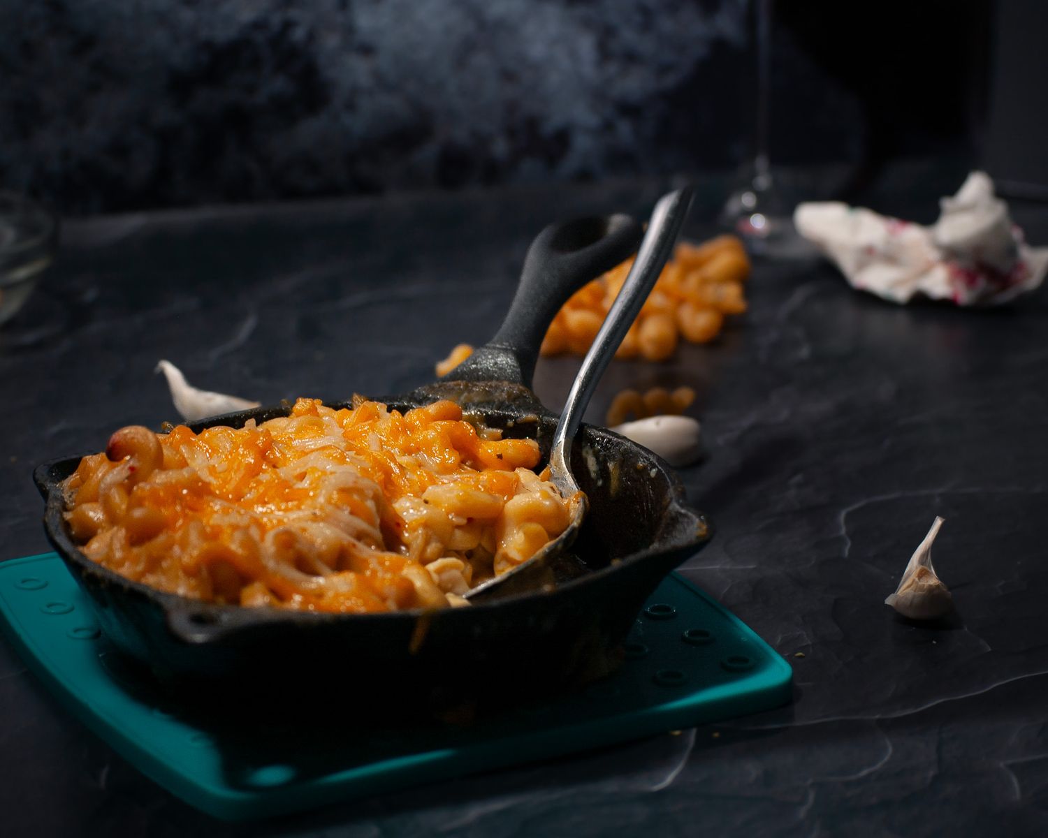 A steaming cast iron skillet filled with baked macaroni and cheese topped with melted cheddar cheese on a teal placemat.
