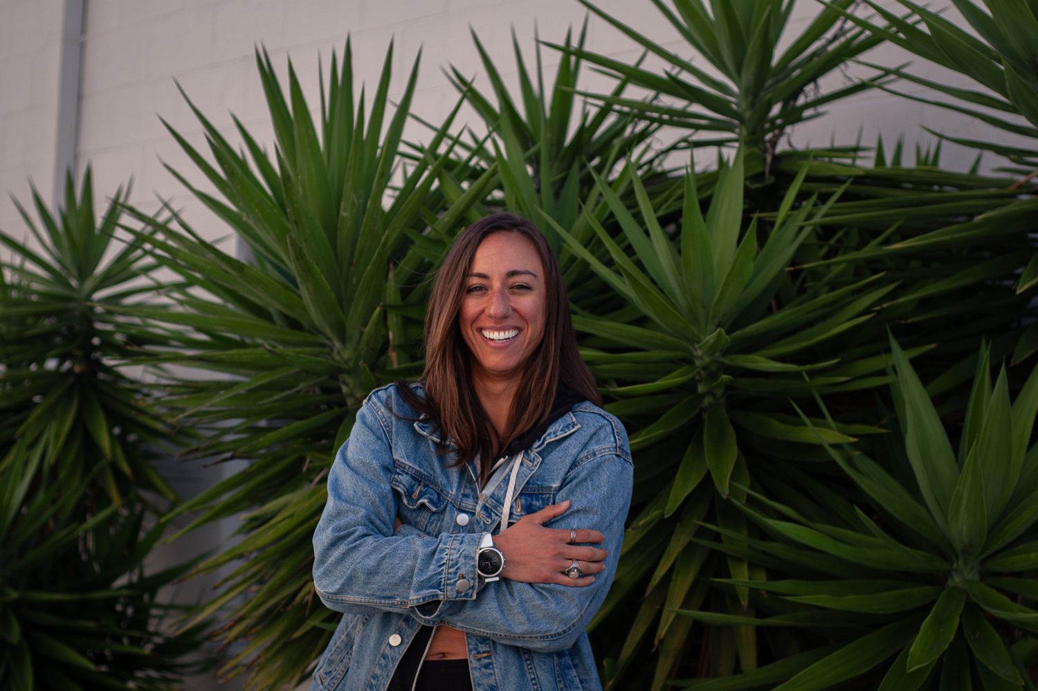A casual portrait in front of lush green yucca plants at dusk wearing a denim jacket.