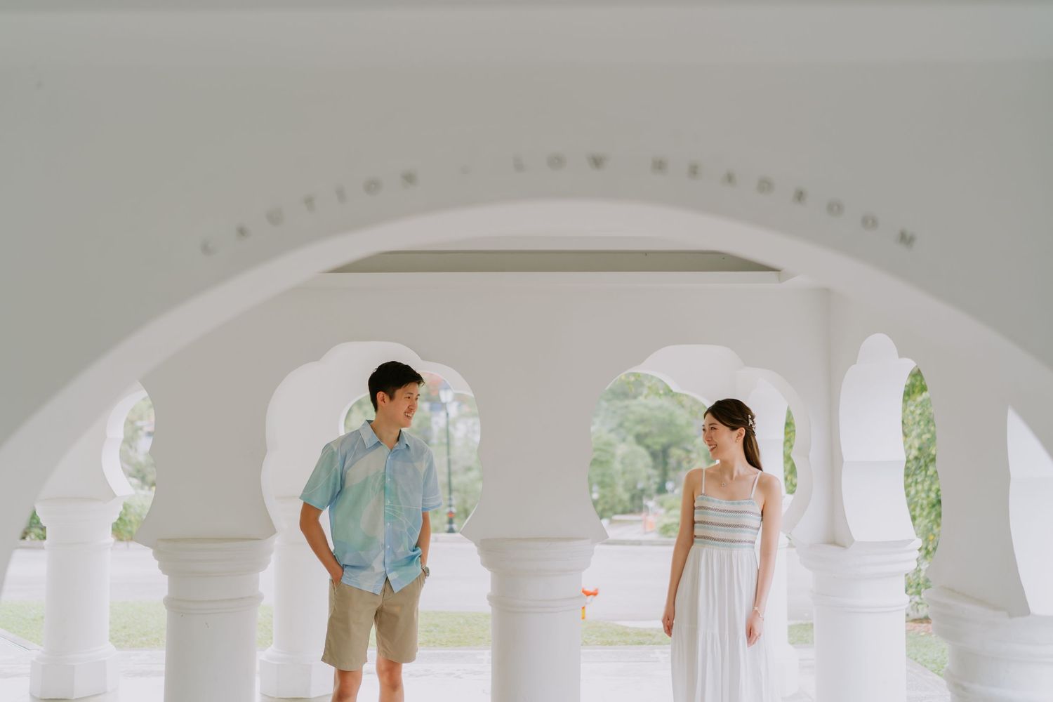Couple posing under elegant white arched columns during outdoor pre-wedding photo session.