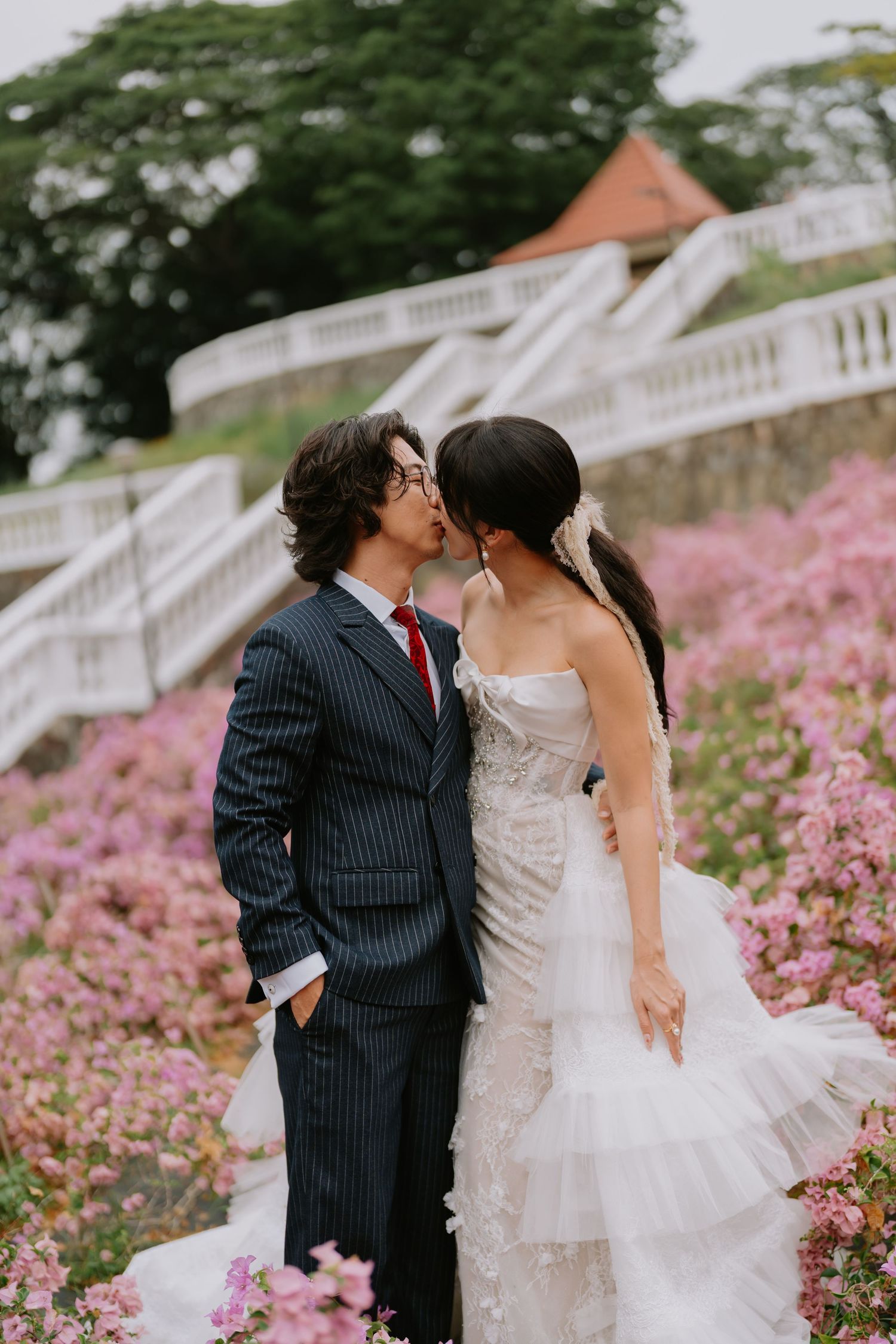 Bride and groom sharing a kiss in a field of pink flowers with white staircase backdrop.