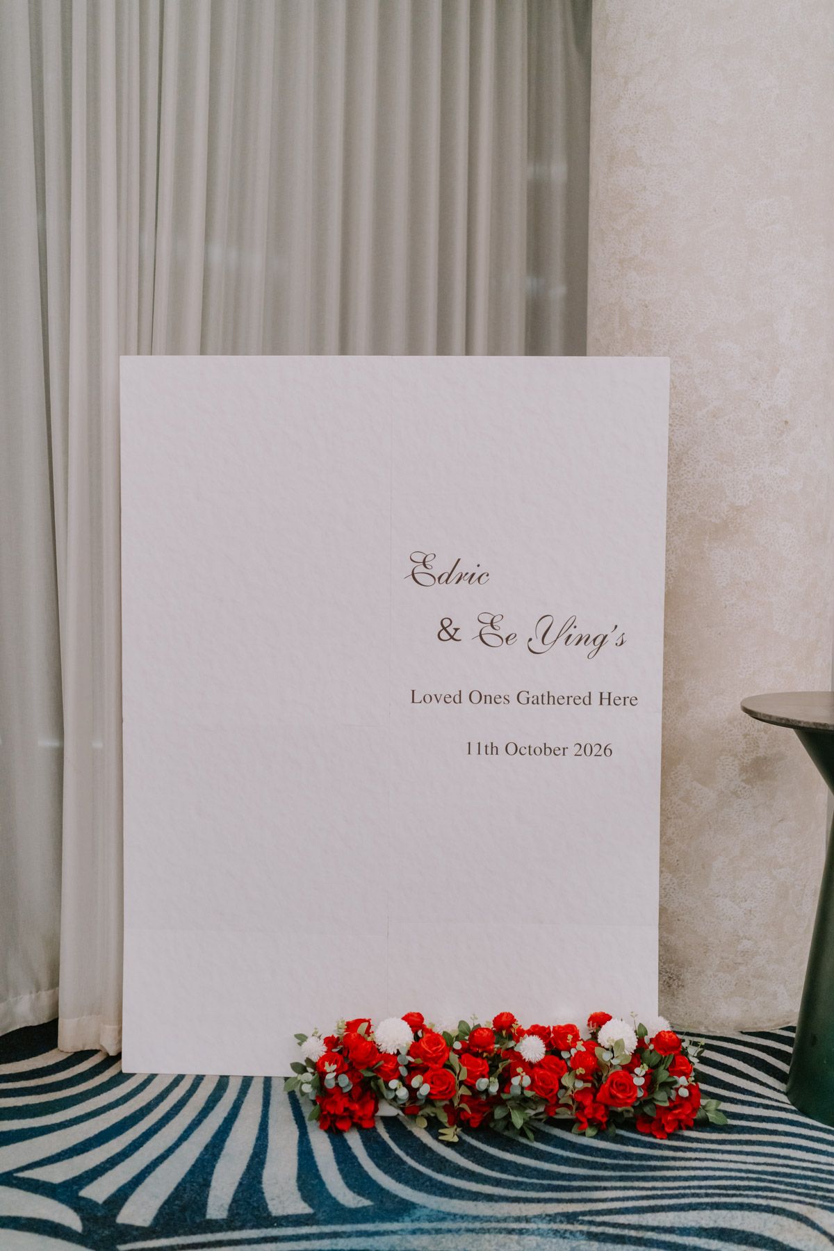 White wedding welcome sign for Edric and Ee Ying decorated with red and white flowers at the base.