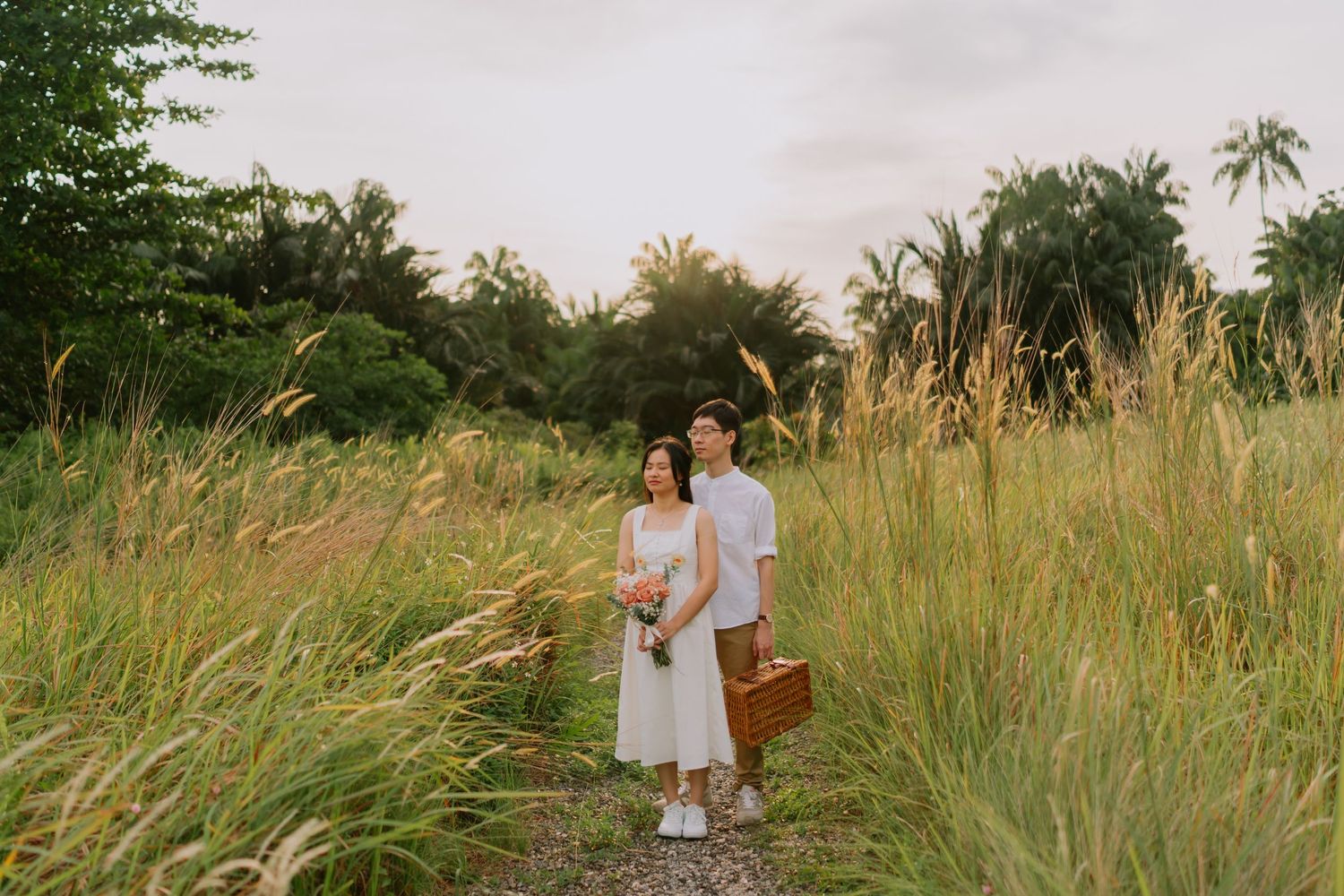 Couple standing together on a path surrounded by tall golden grass at golden hour sunset.